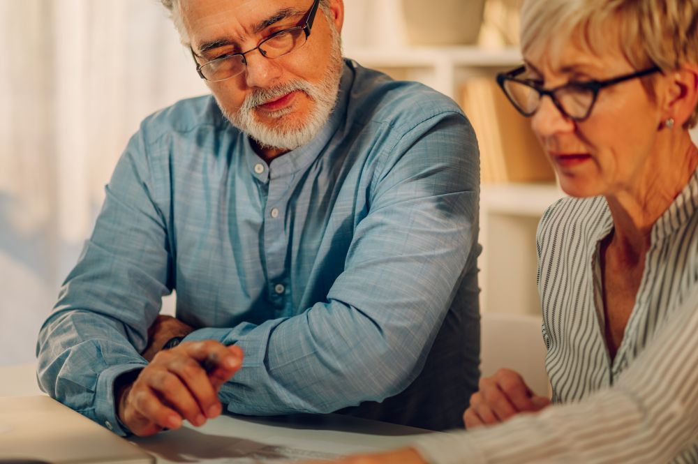 A man in glasses points at a document, discussing with a couple at a table.