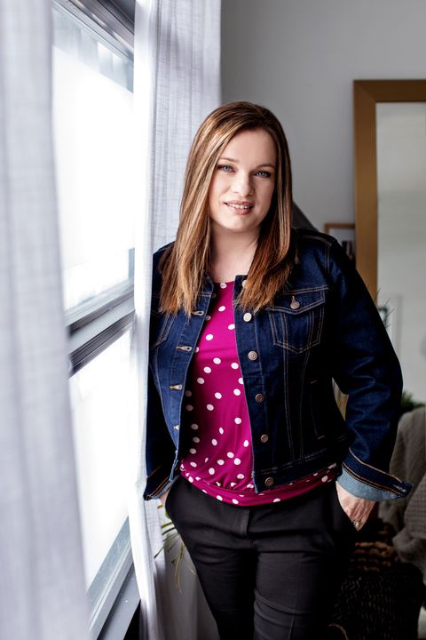 A woman in a denim jacket is leaning against a window.