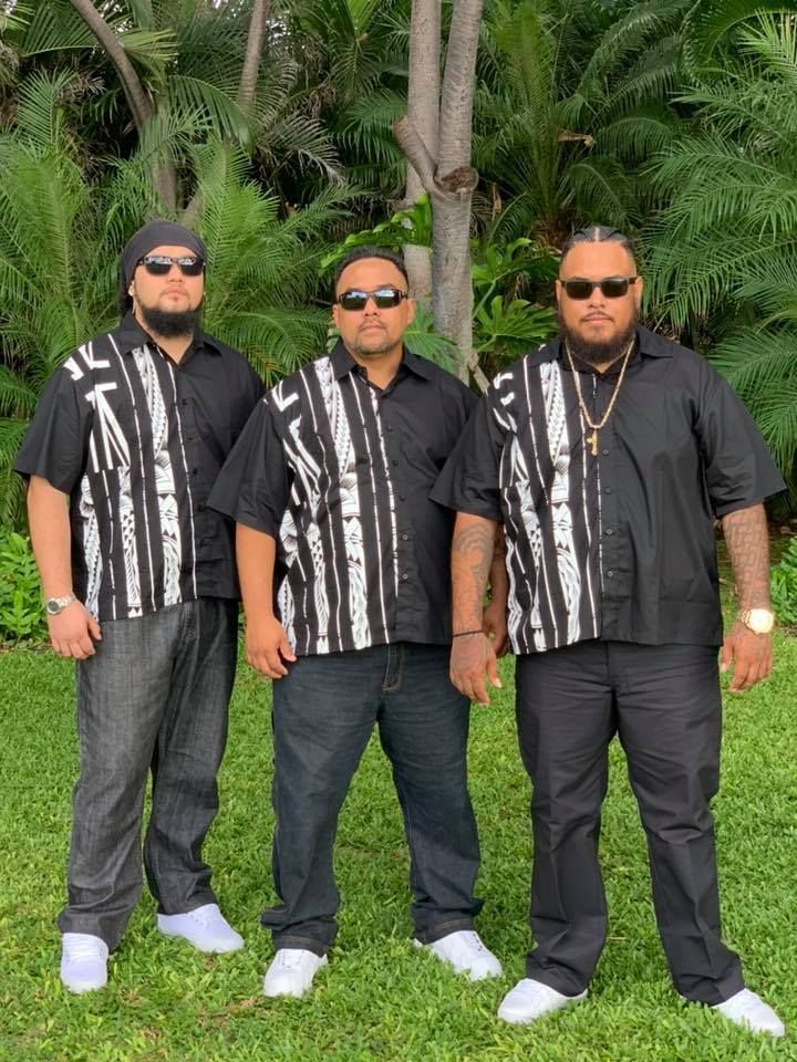 Three men wearing black shirts and sunglasses are standing in the grass.