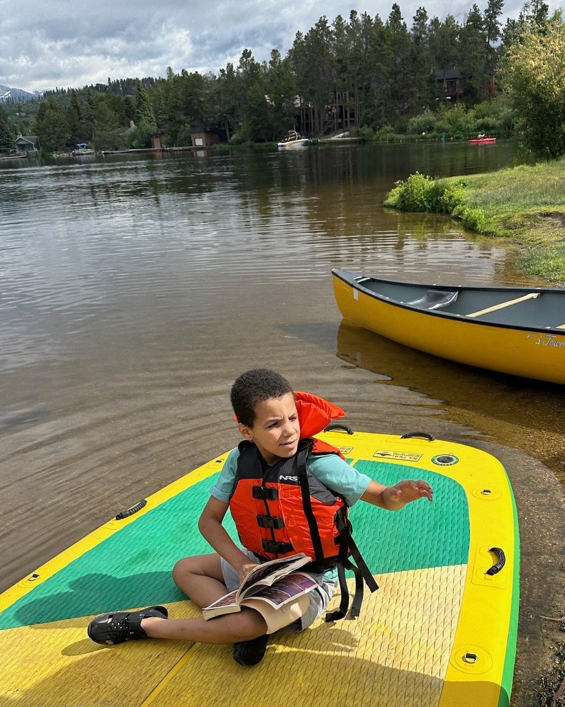 A young boy is sitting on a paddle board near a lake.