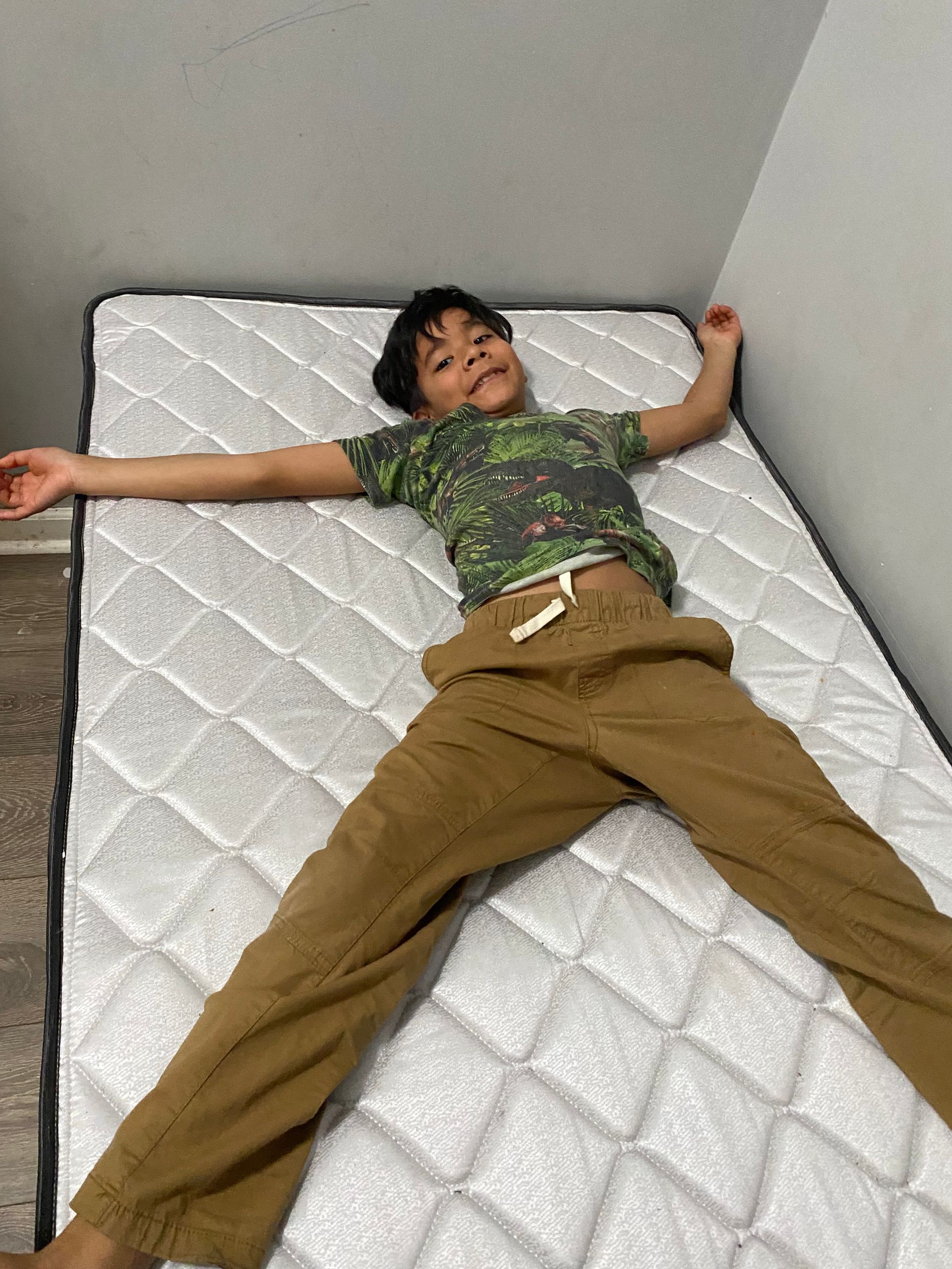 A young boy is laying on a mattress in a bedroom.