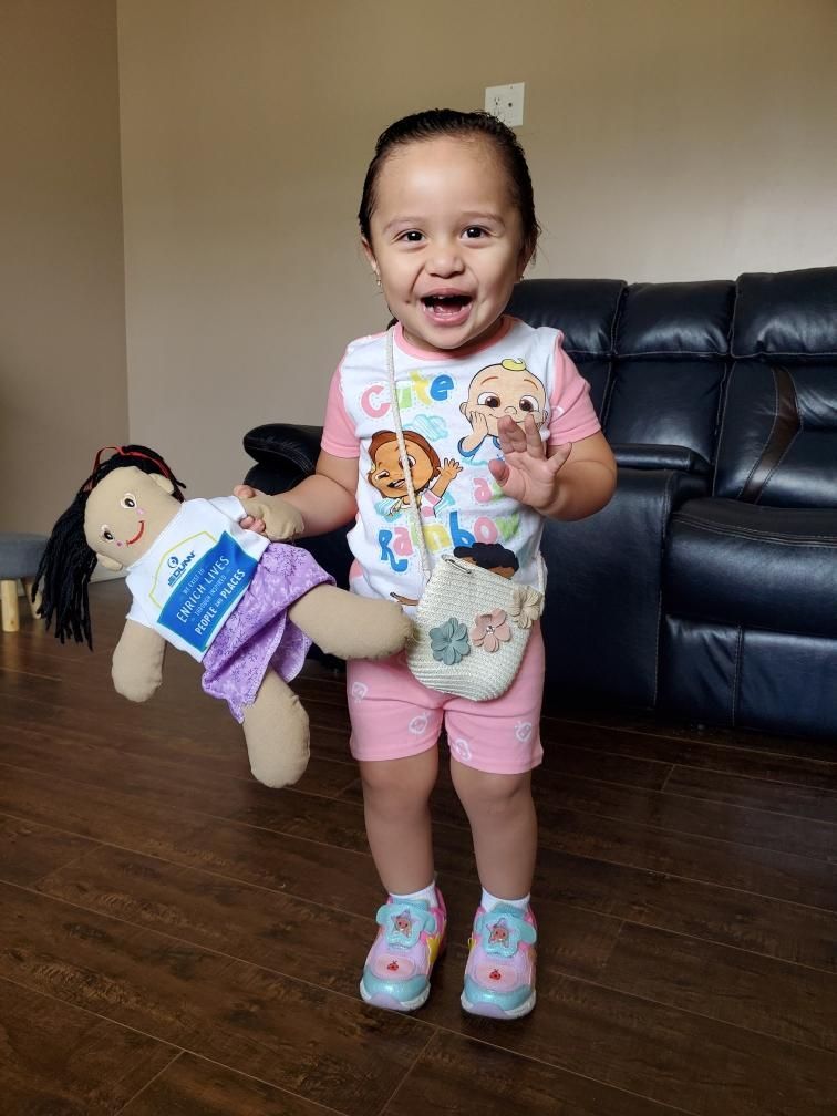 A little girl is holding a stuffed doll and a purse.