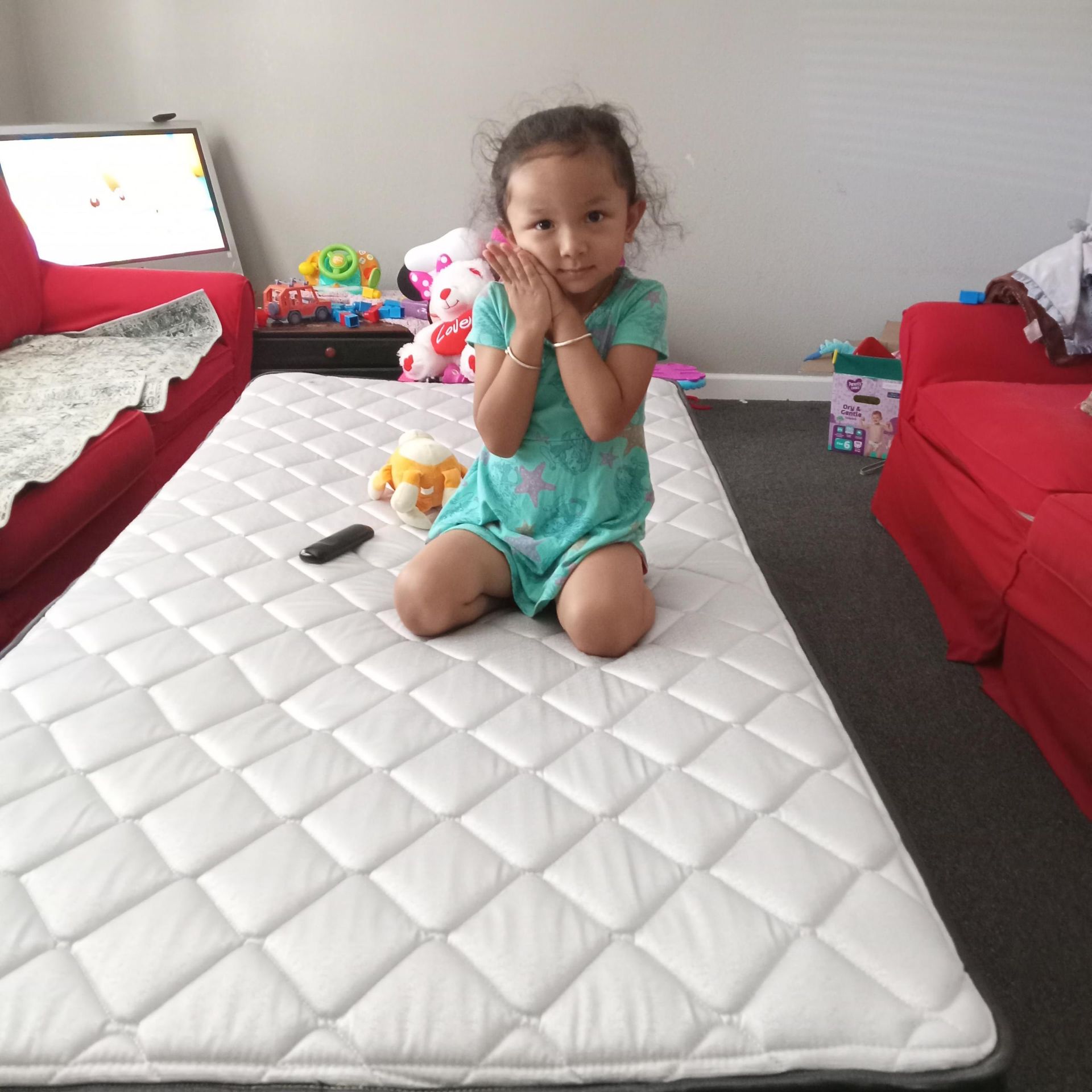 A little girl is kneeling on a mattress in a living room