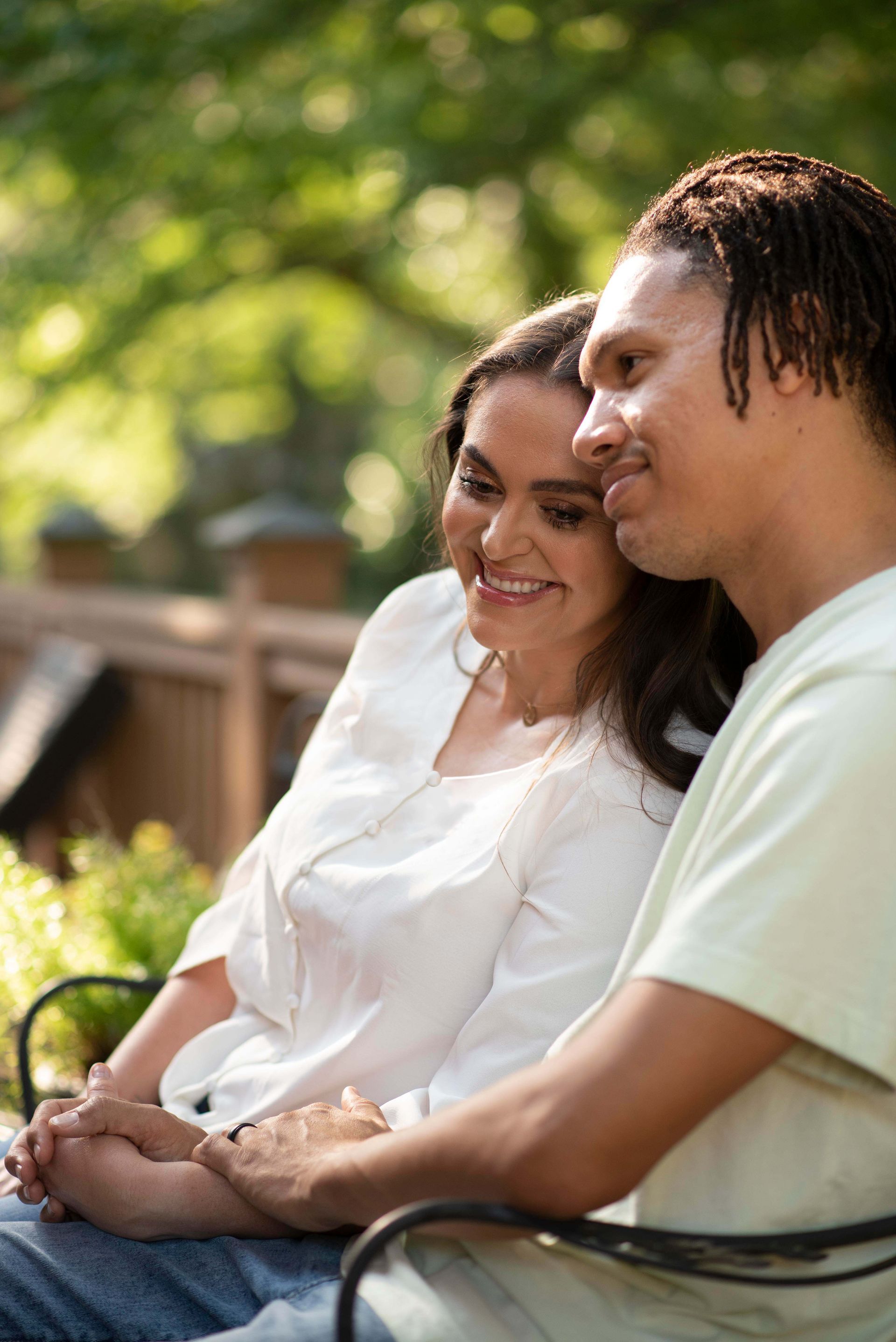 A man and a woman are sitting on a bench holding hands and smiling.