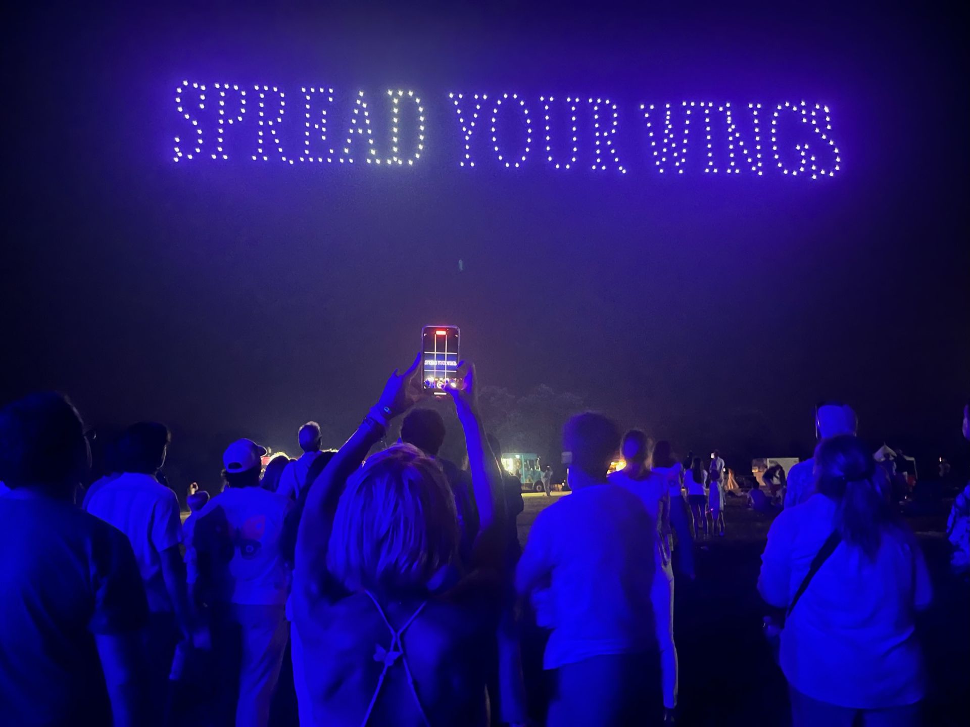 A group of people are standing in front of a sign that says spread your wings.