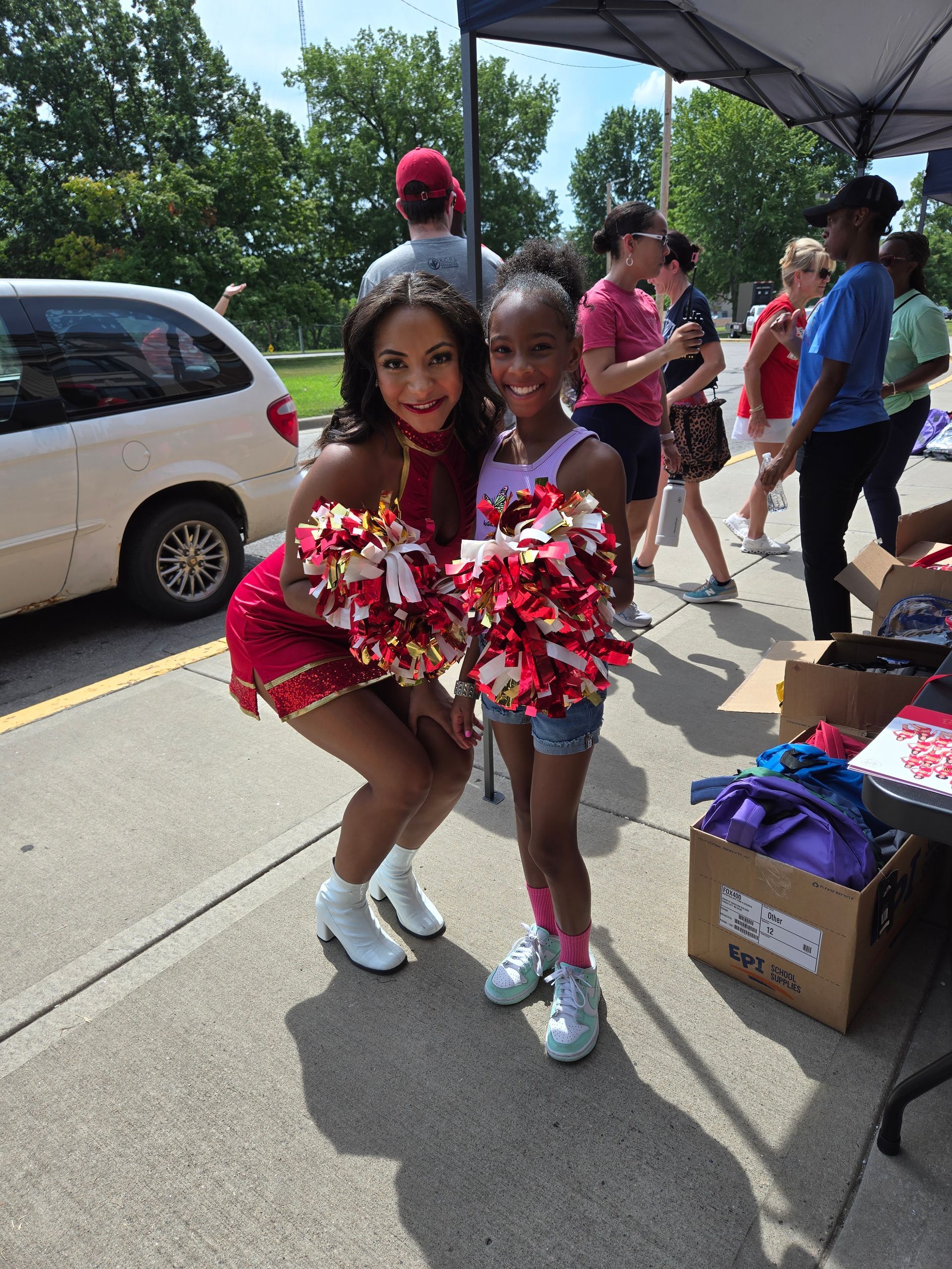 Two cheerleaders are posing for a picture on the sidewalk.