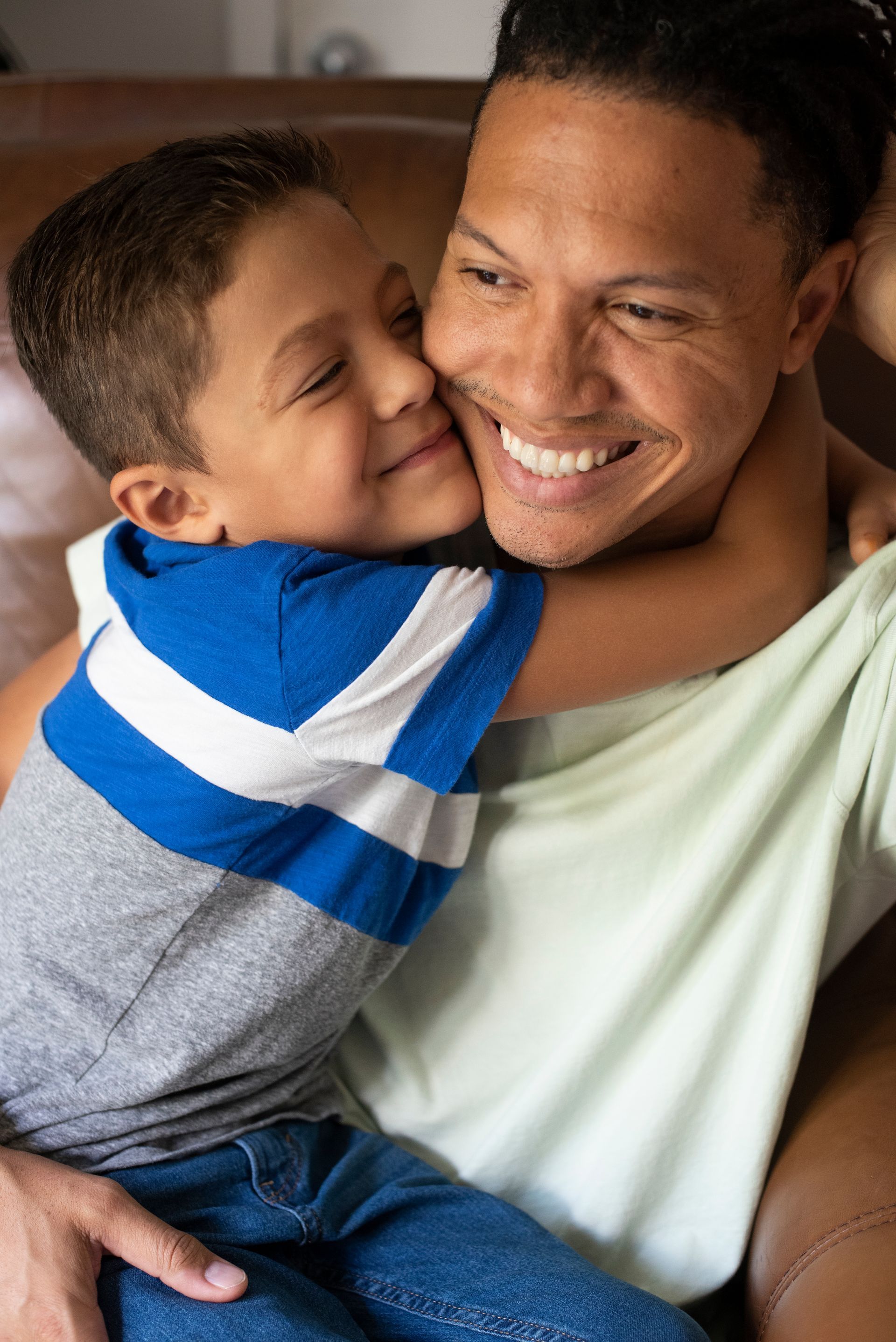 A man is holding a young boy in his arms and the boy is kissing the man on the cheek.