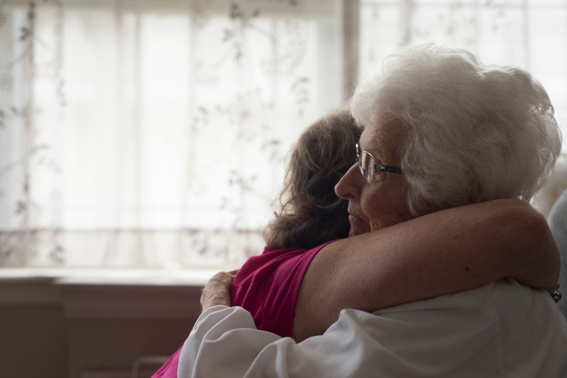 An elderly woman is hugging a young girl in a hospital bed.