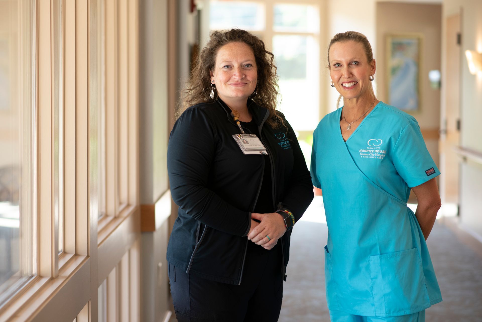 Two nurses are standing next to each other in a hallway.