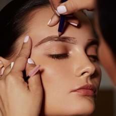 Person getting their eyebrow shaped with a pencil; close-up of face and hand.