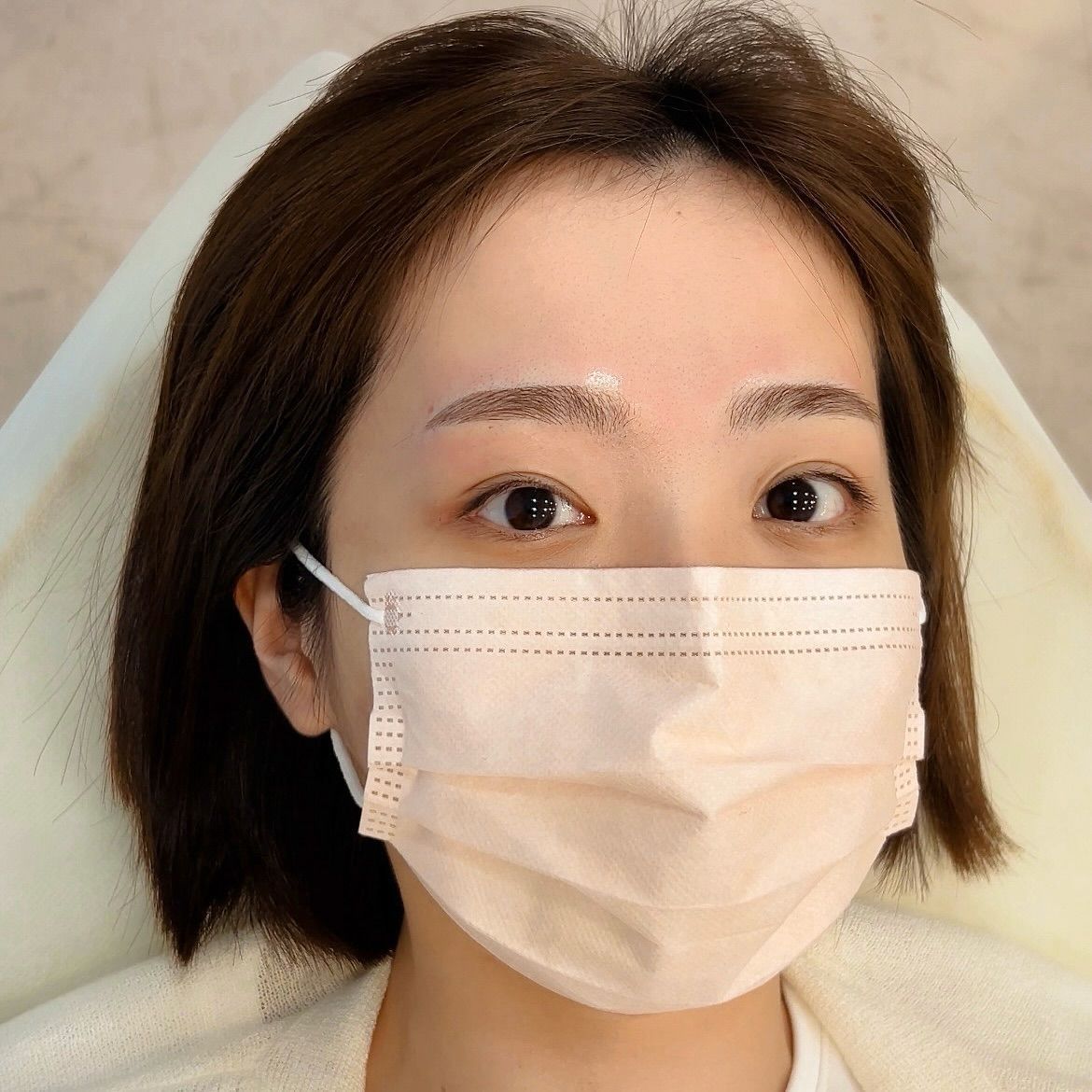 Woman with a face mask, light skin, short brown hair, looking at the camera.