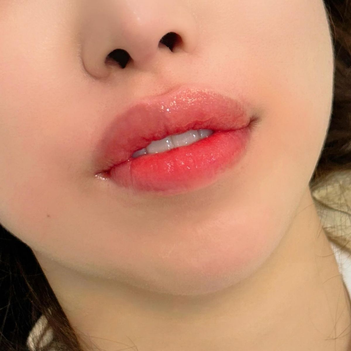 Close-up of a person's lips. The lips are glossy red with visible teeth, and the skin is fair.