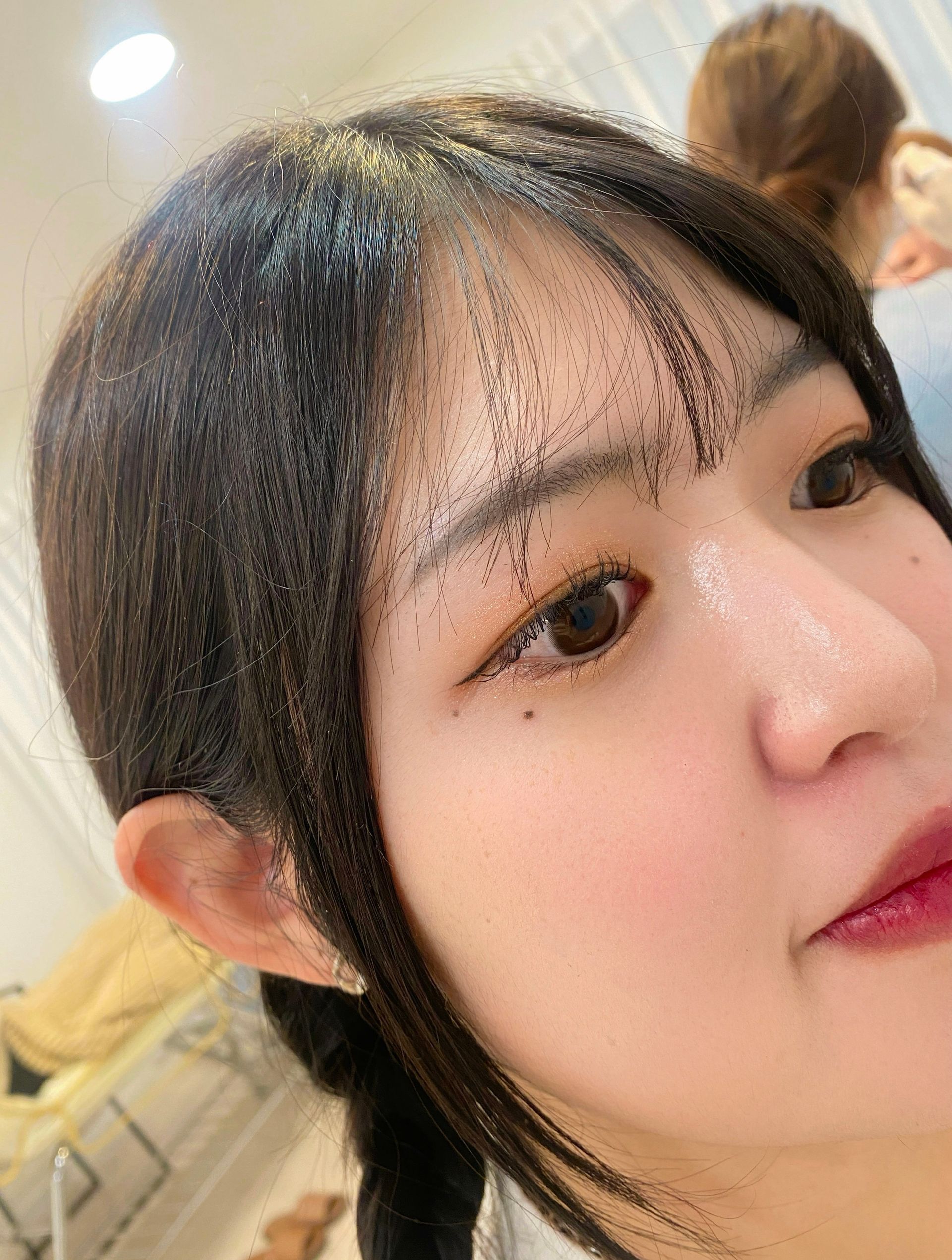 Woman with dark hair, bangs, and light makeup; close-up, angled face, indoors.