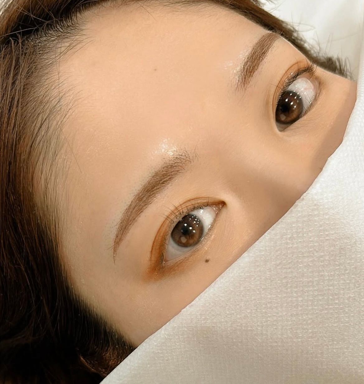 Eyes peeking from behind white fabric, with warm eyeshadow and visible eyebrows.