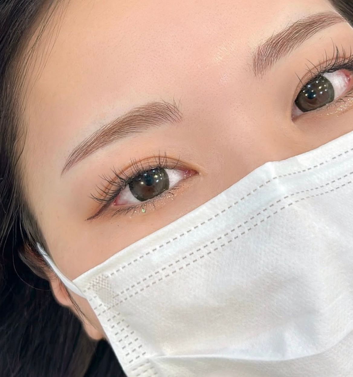 Close-up of a person's eyes, eyebrows, and lower face wearing a white mask.