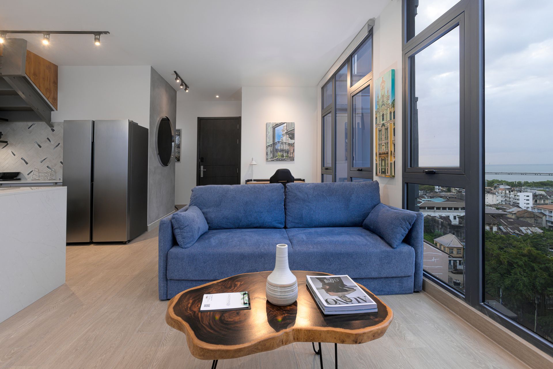 Living room with blue sofa, wooden coffee table, and large window overlooking a city.