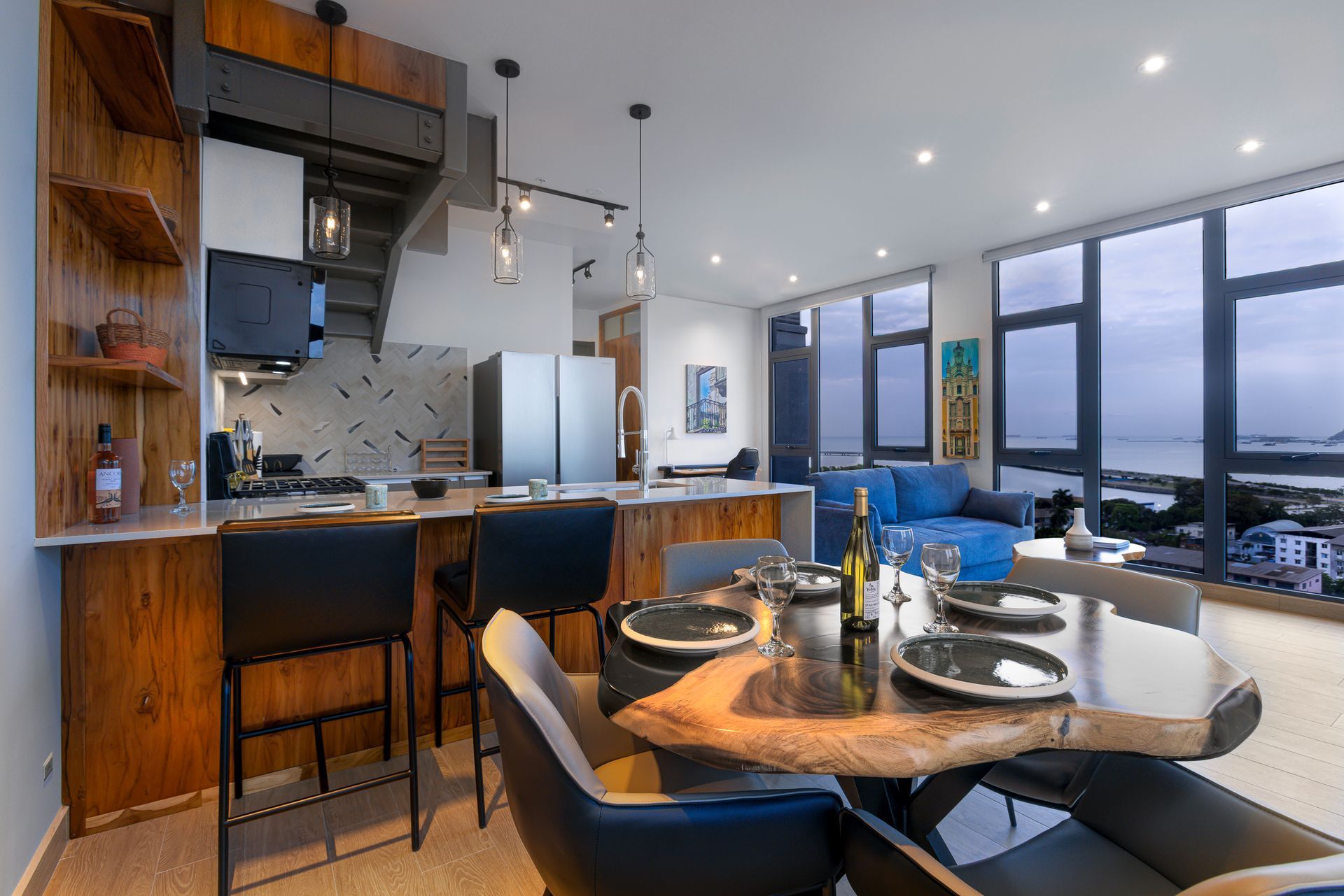 Modern kitchen and dining area with wooden accents, island, and large windows with a view.