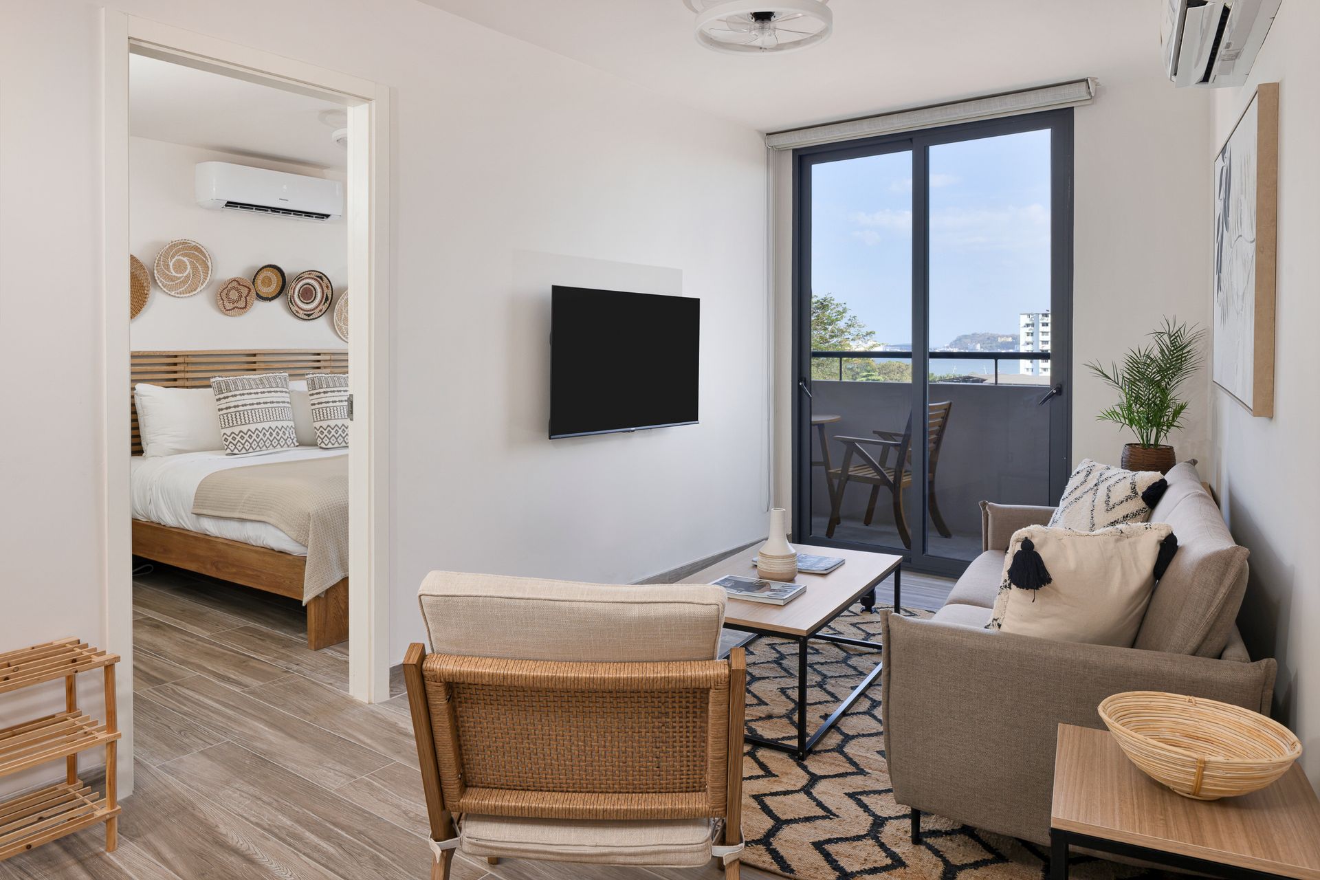 Cozy apartment interior with living area, balcony, and bedroom visible. Neutral tones, natural light, and modern decor.