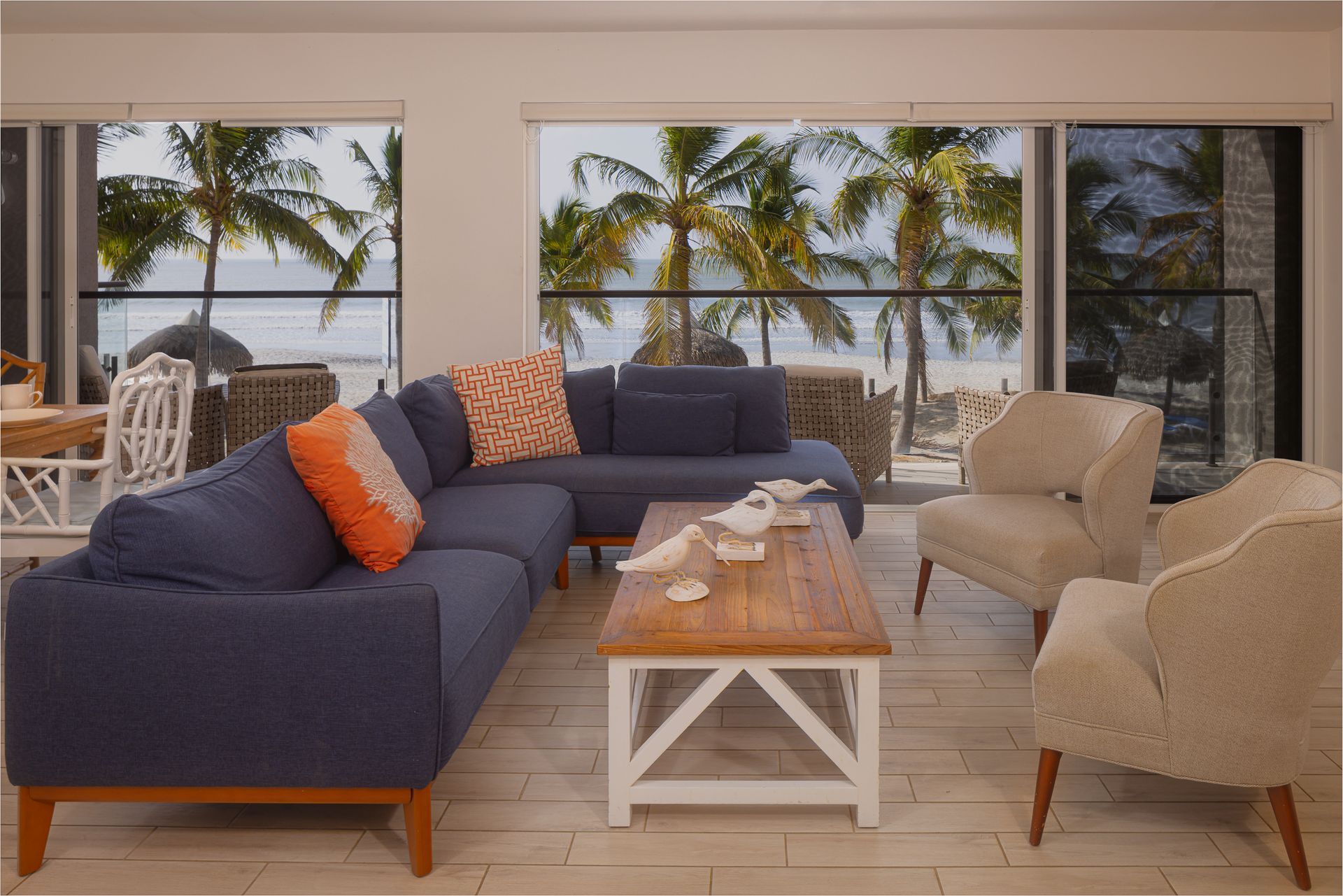 Living room with ocean view, blue sectional sofa, two beige armchairs, and wooden coffee table.