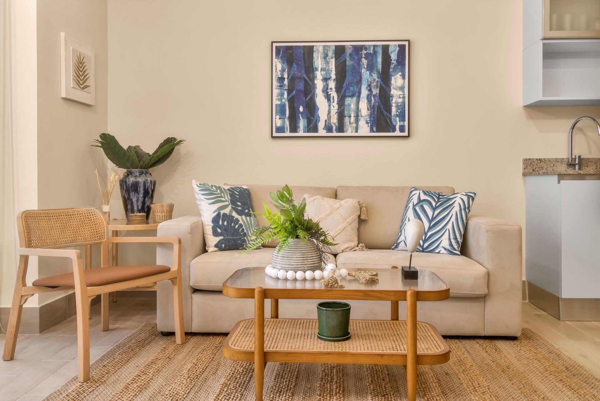 Living room with beige sofa, artwork, plants, and wicker chair.