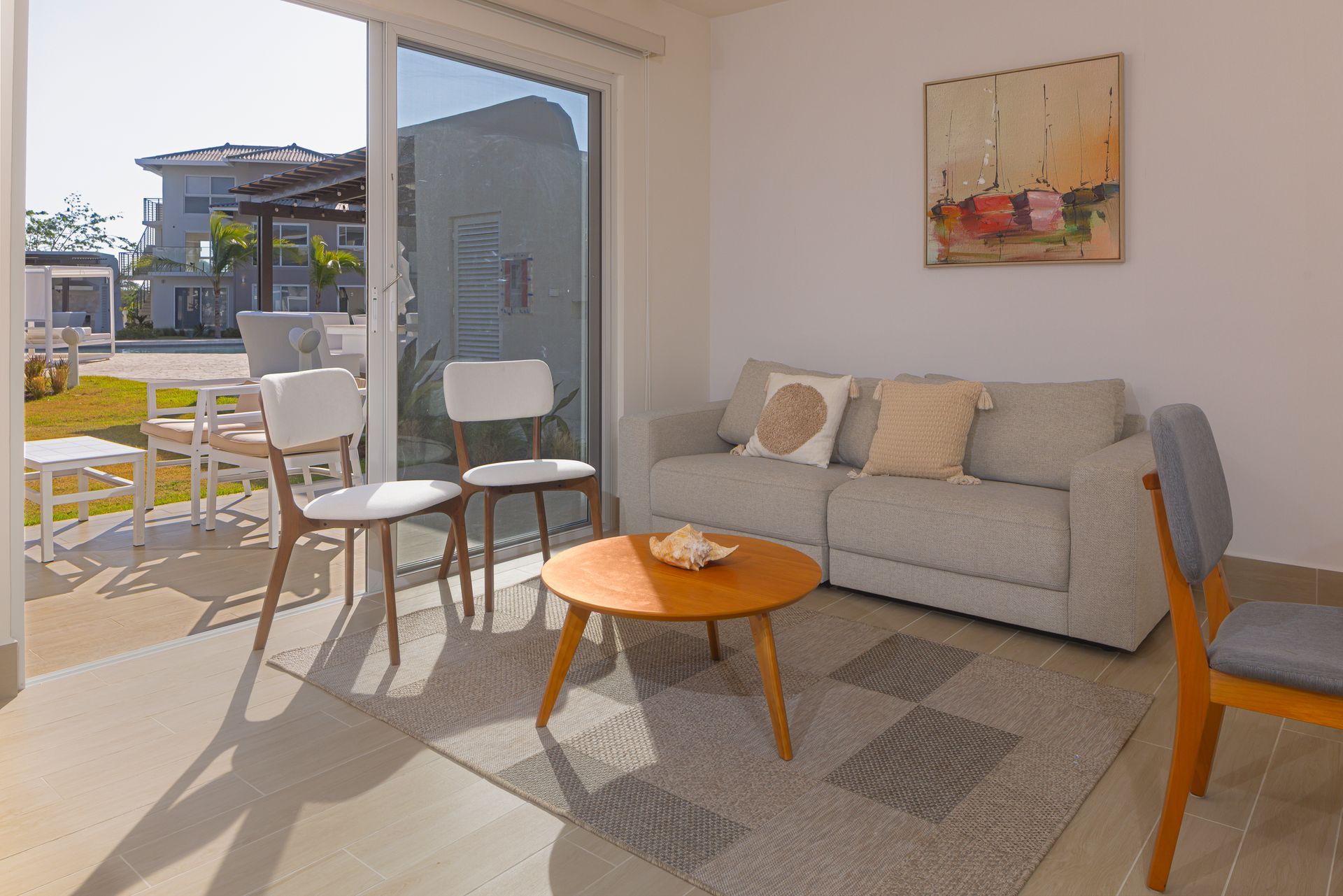 Living room with gray sofa, round wooden coffee table, and two chairs near sliding glass door.