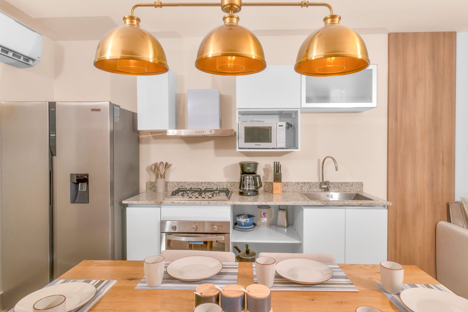 Kitchen with white cabinets, gold light fixtures, appliances, and a table set for two.