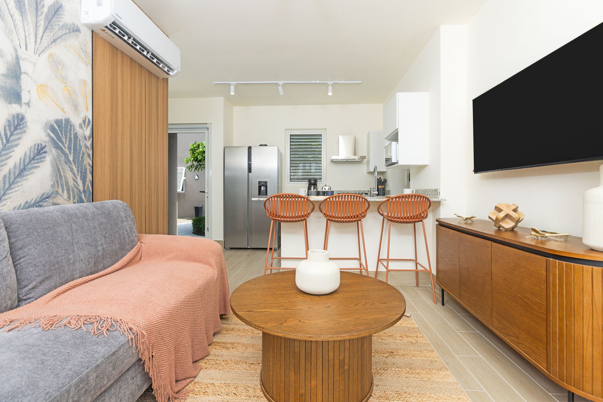Living room with gray sofa, wooden furniture, and open kitchen with bar stools.