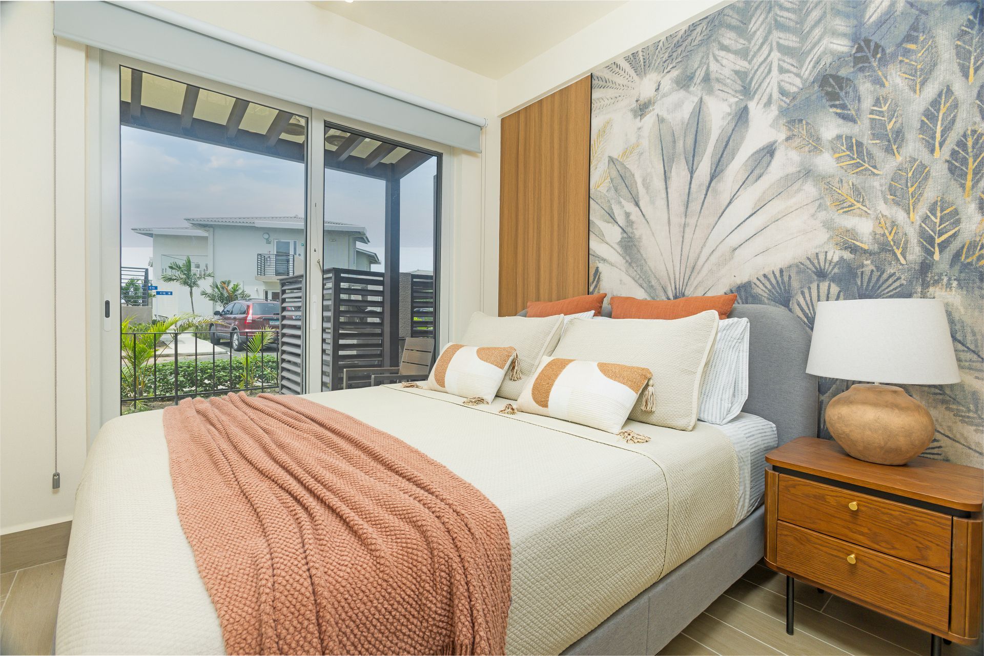 Bedroom with bed, patterned wall, large window, and wooden nightstand.