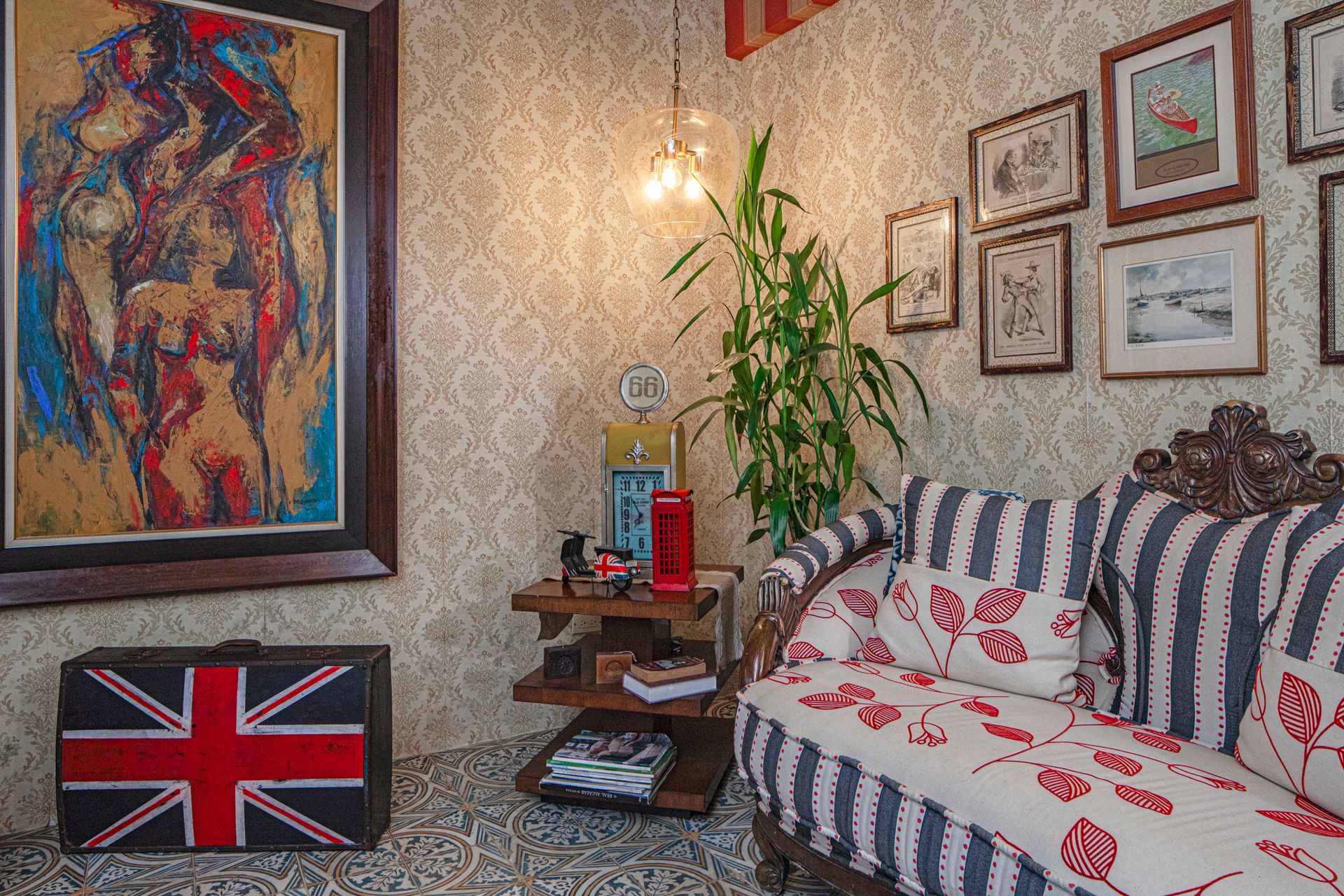 Living room with patterned wallpaper, striped couch, artwork, Union Jack suitcase, and gallery wall.