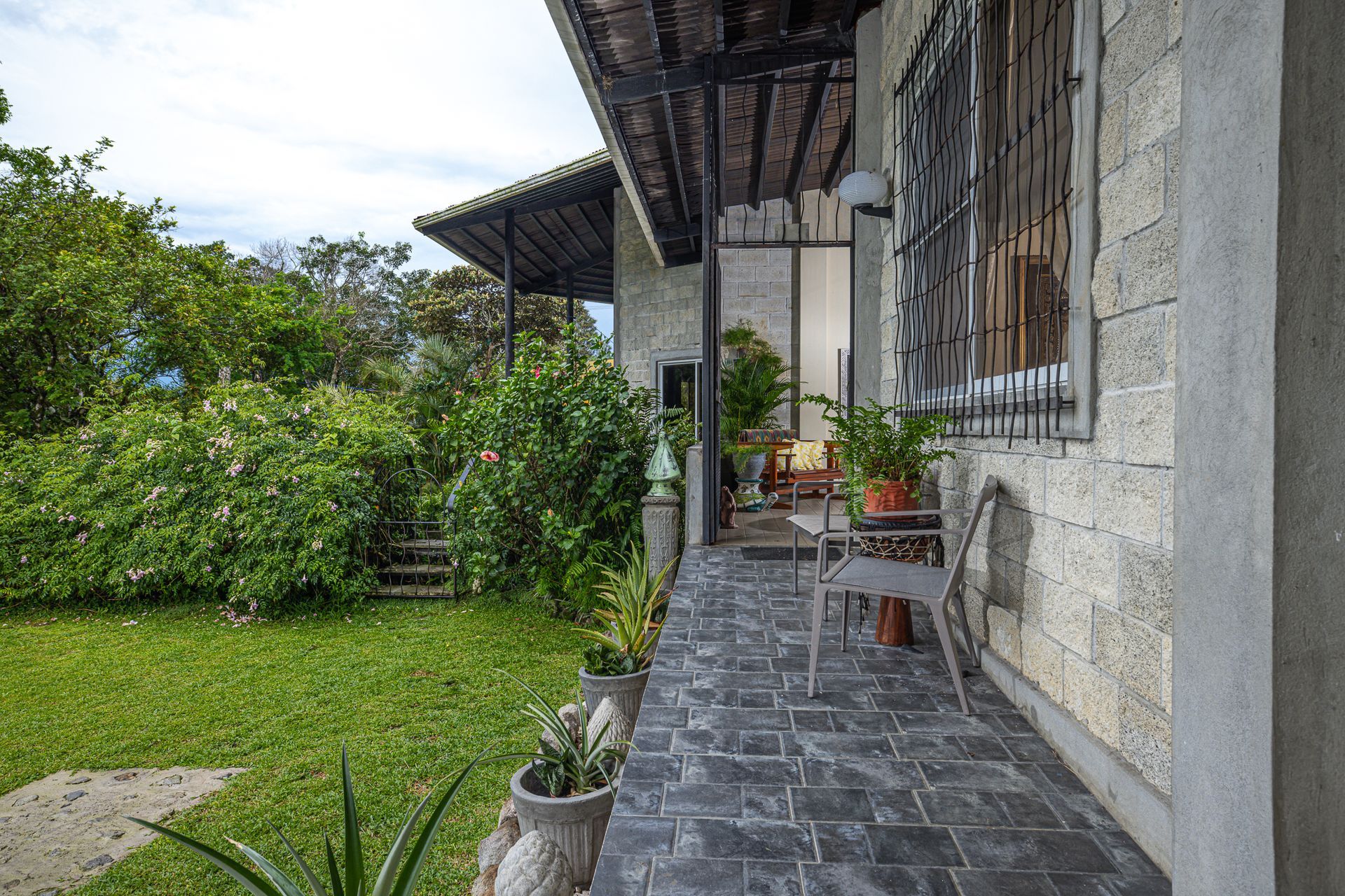 Stone house porch with brick walkway, potted plants, and green yard.