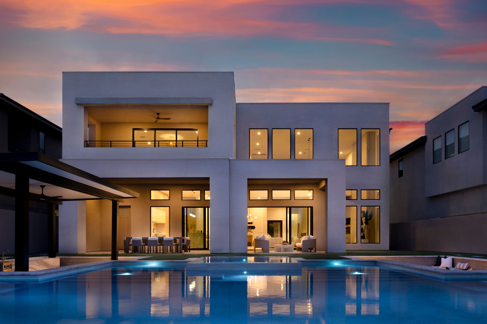 Modern two-story house with pool at dusk; exterior lit windows, sky with pink and orange hues.