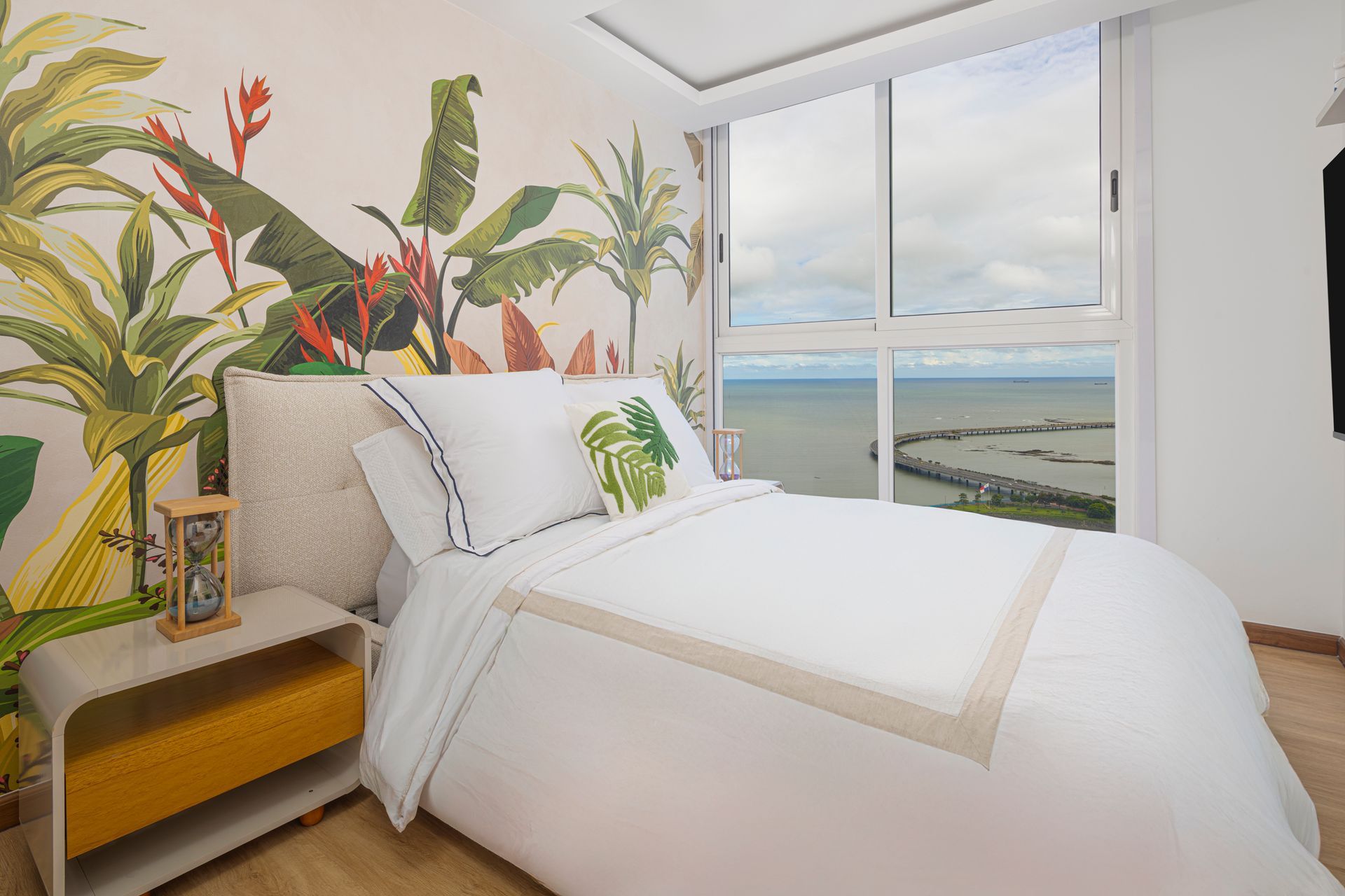 Bedroom with white bedding, floral mural, large window with ocean view.