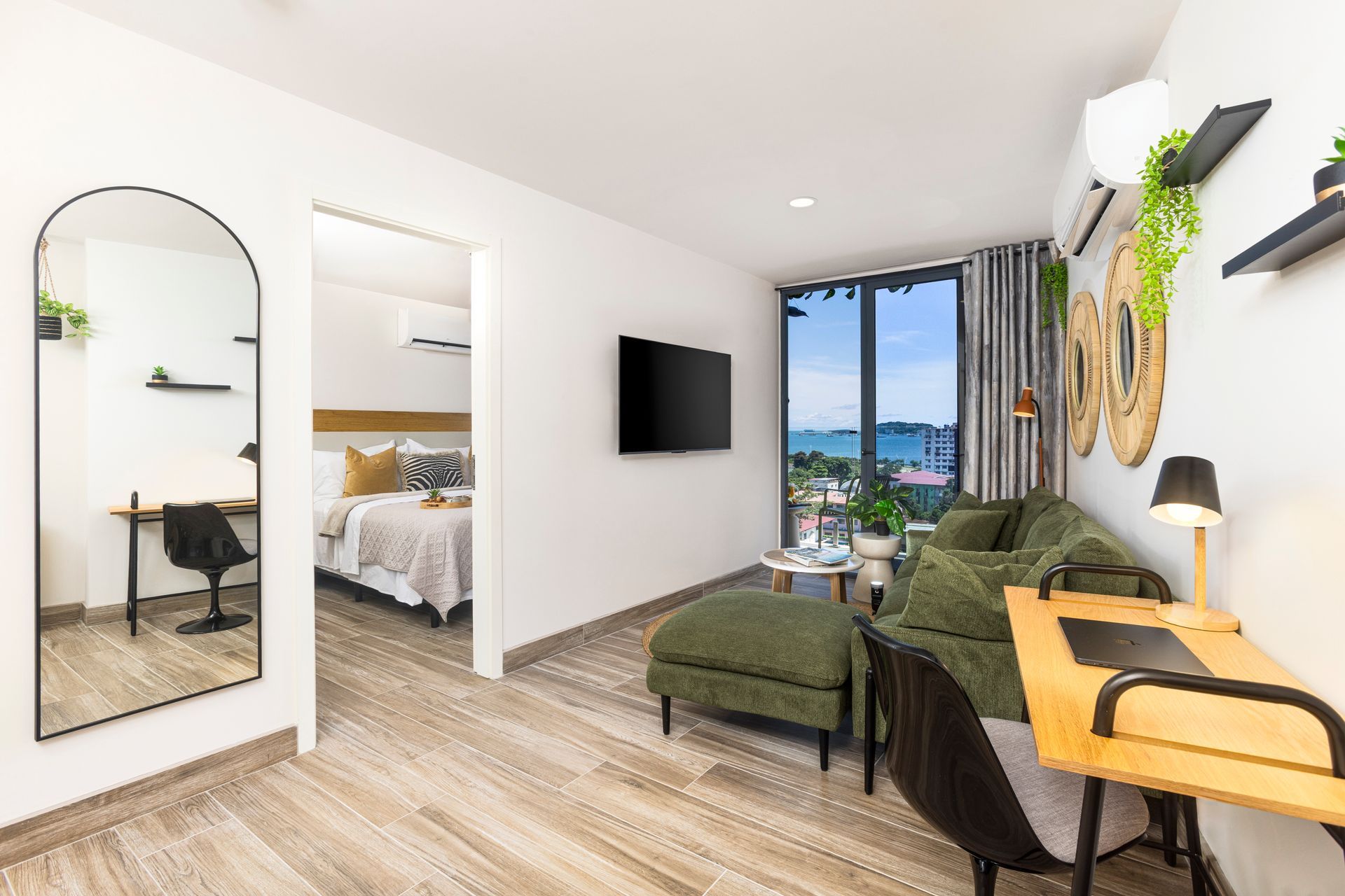 Modern studio apartment with olive green sofa, work desk, and bedroom view.