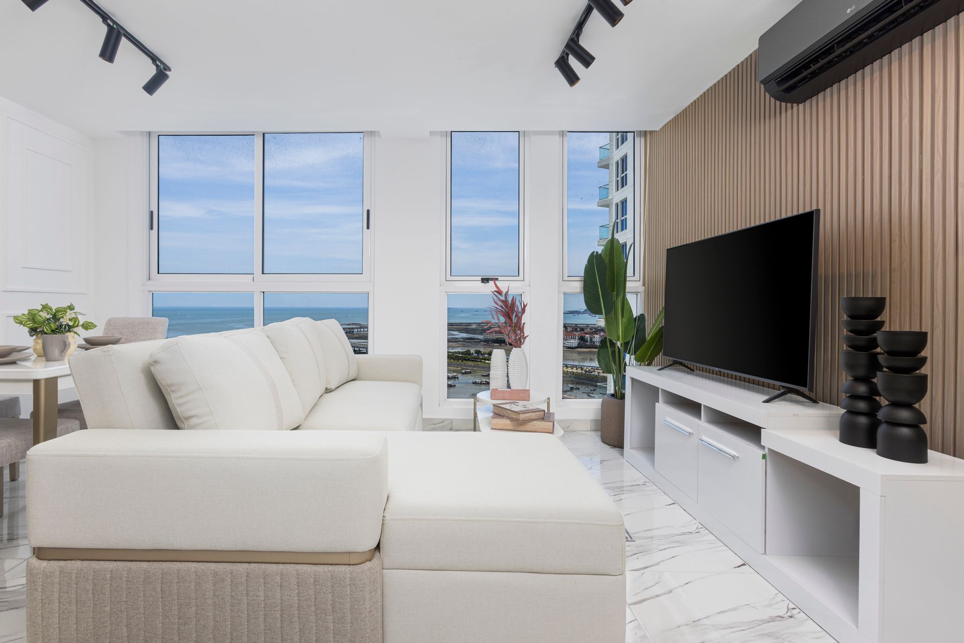 Living room with ocean view, white sectional sofa, TV, and wooden accent wall.