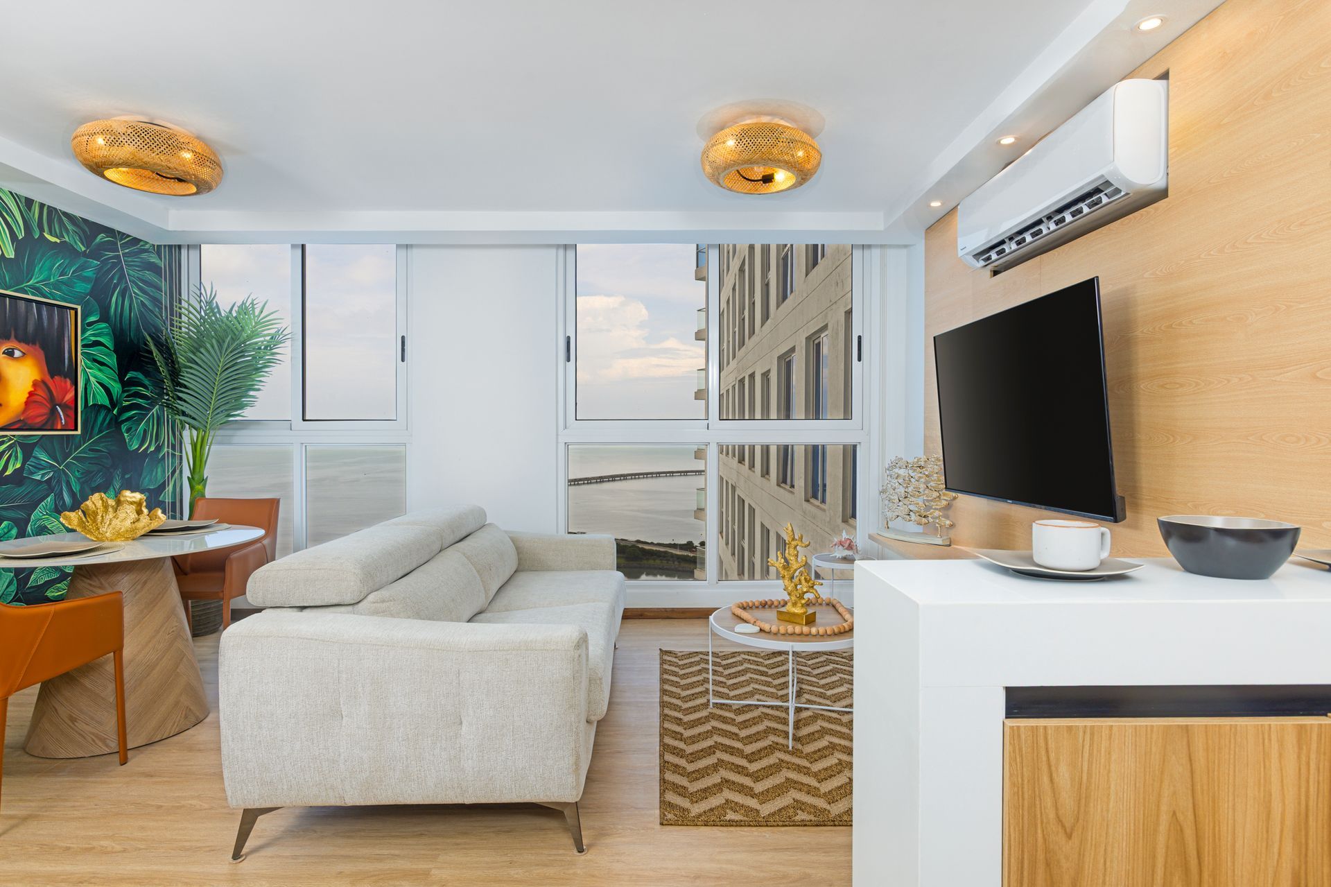 Living room with white sofa, gold accents, and ocean view through windows.