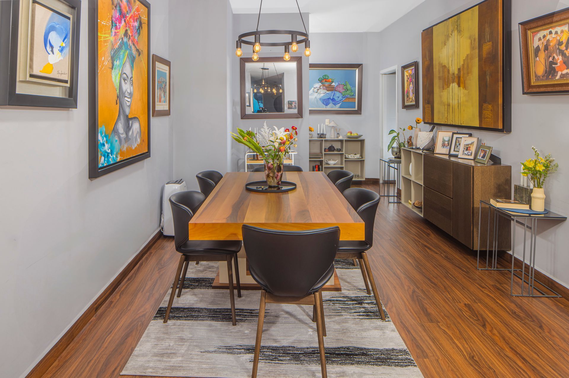 Dining room with wooden table, black chairs, artwork on gray walls, and area rug.