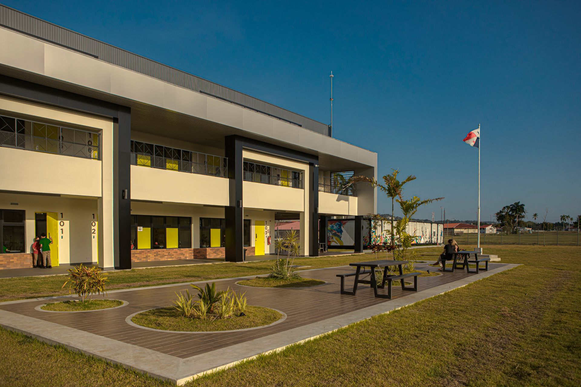 Modern two-story building with tan walls and black trim, a Panamanian flag, and a grassy lawn.