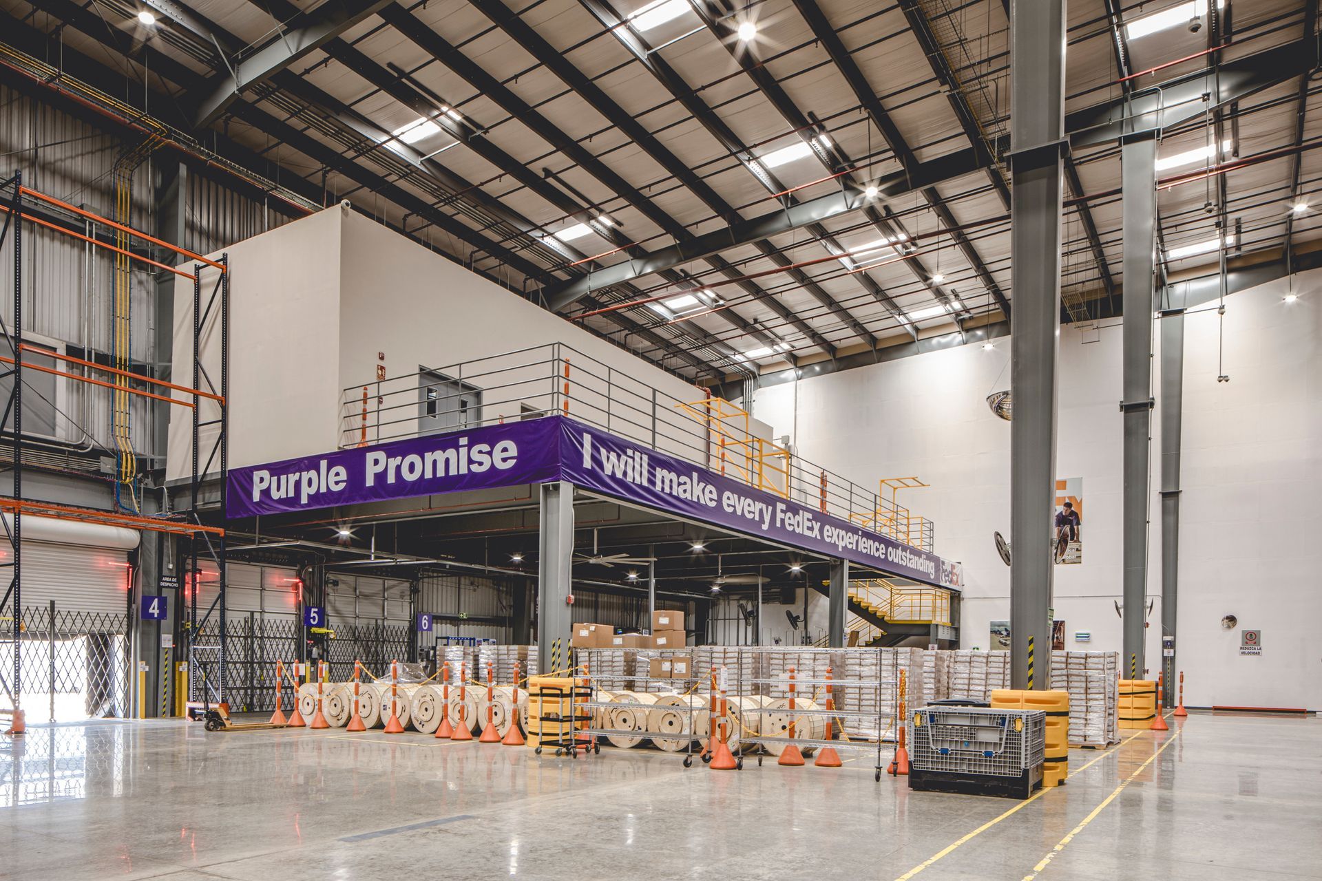 Warehouse interior with a raised platform, purple signage. Loading equipment on the ground floor, industrial setting.