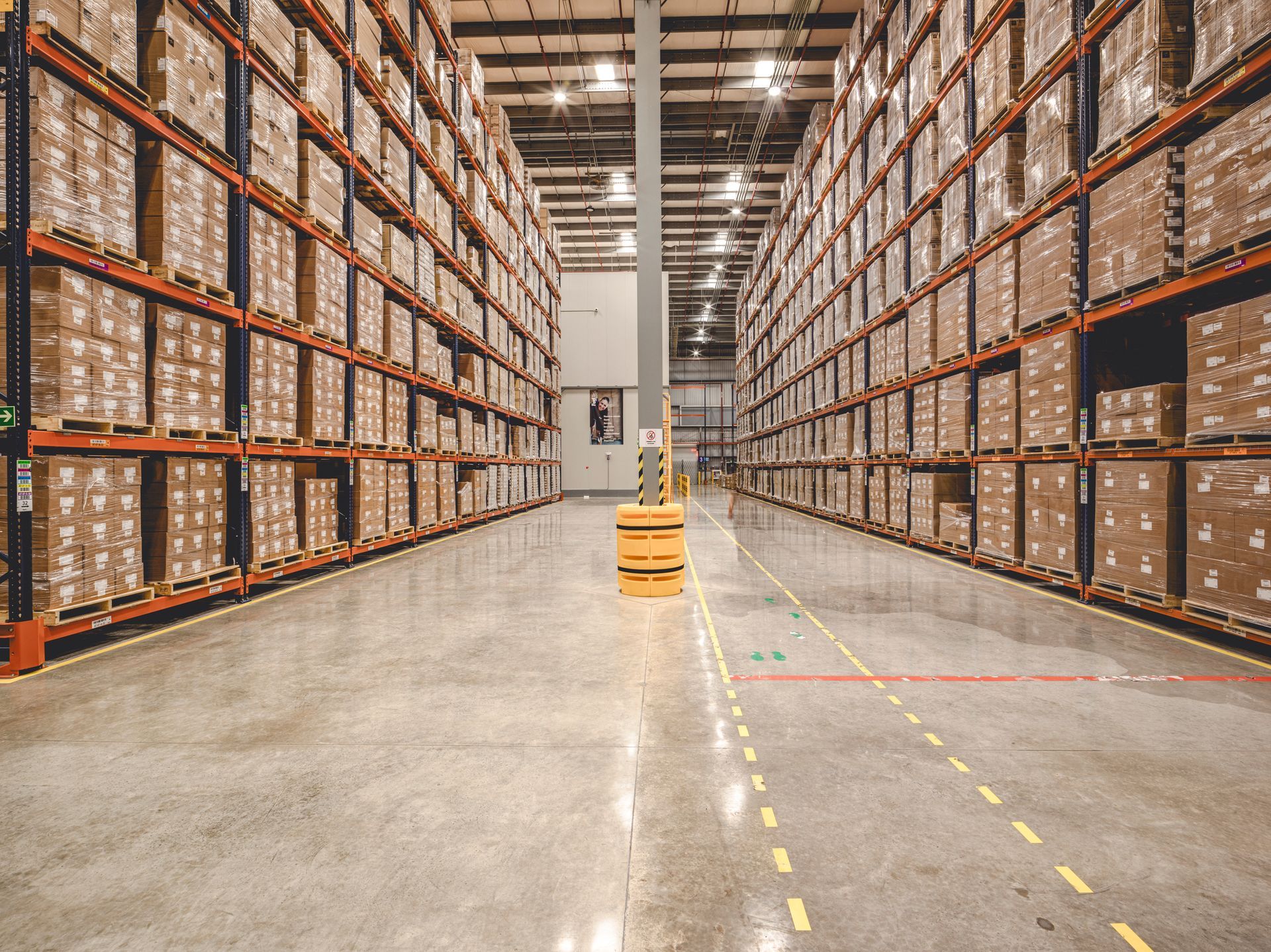 Warehouse interior with tall shelves packed with boxes, a yellow automated guided vehicle, and concrete floor.