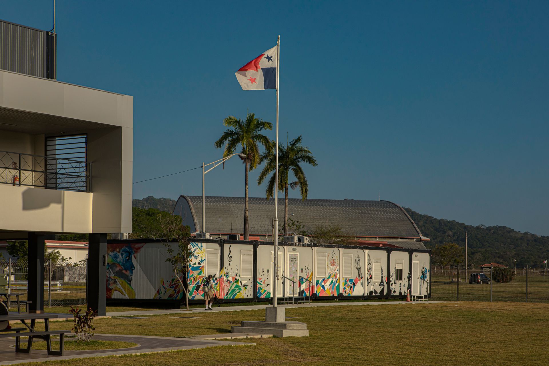 Panamanian flag waving in front of a modern building with a mural and palm trees, clear sky.