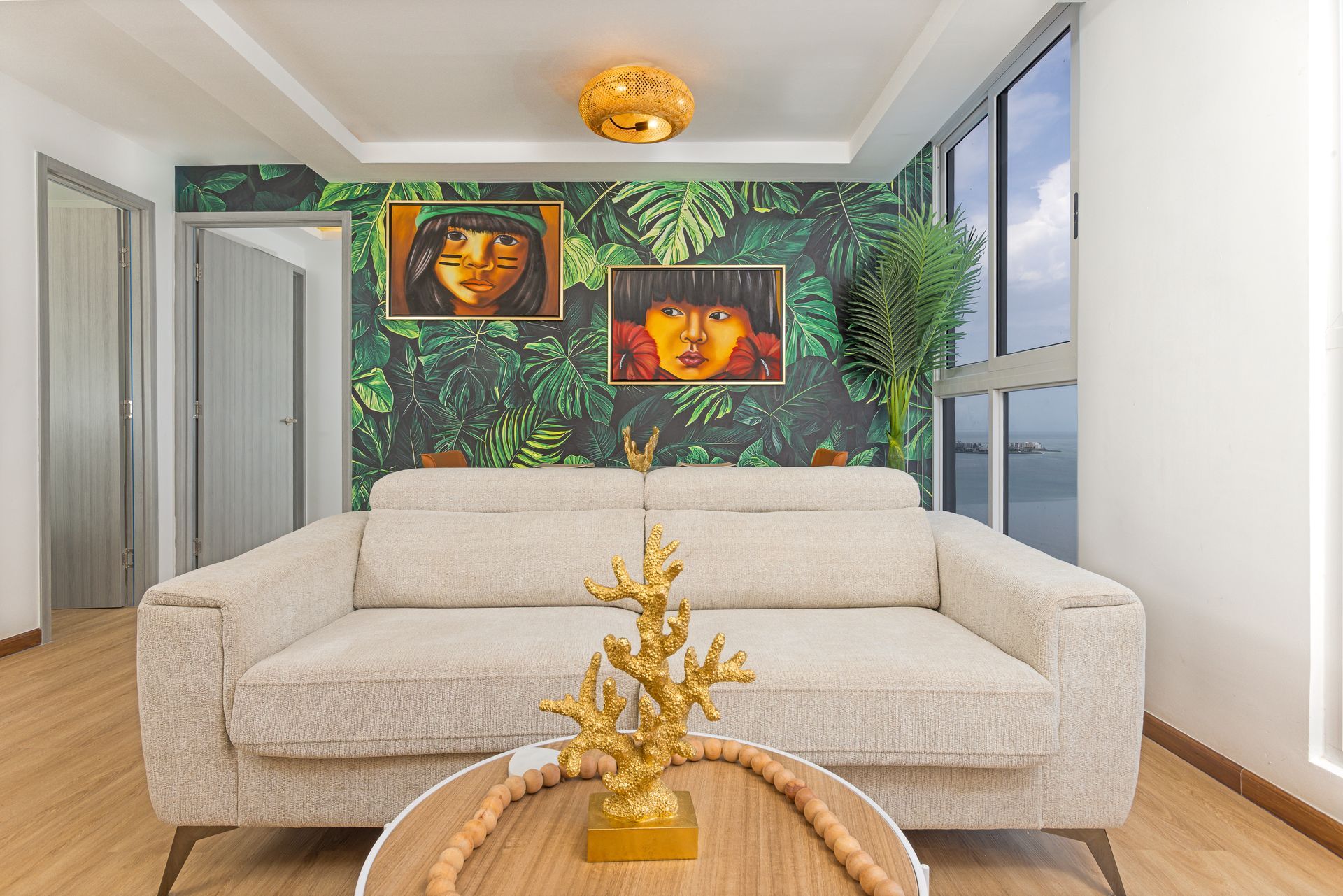 Living room with a beige sofa, two paintings on a green leaf-patterned wall, and a round coffee table.