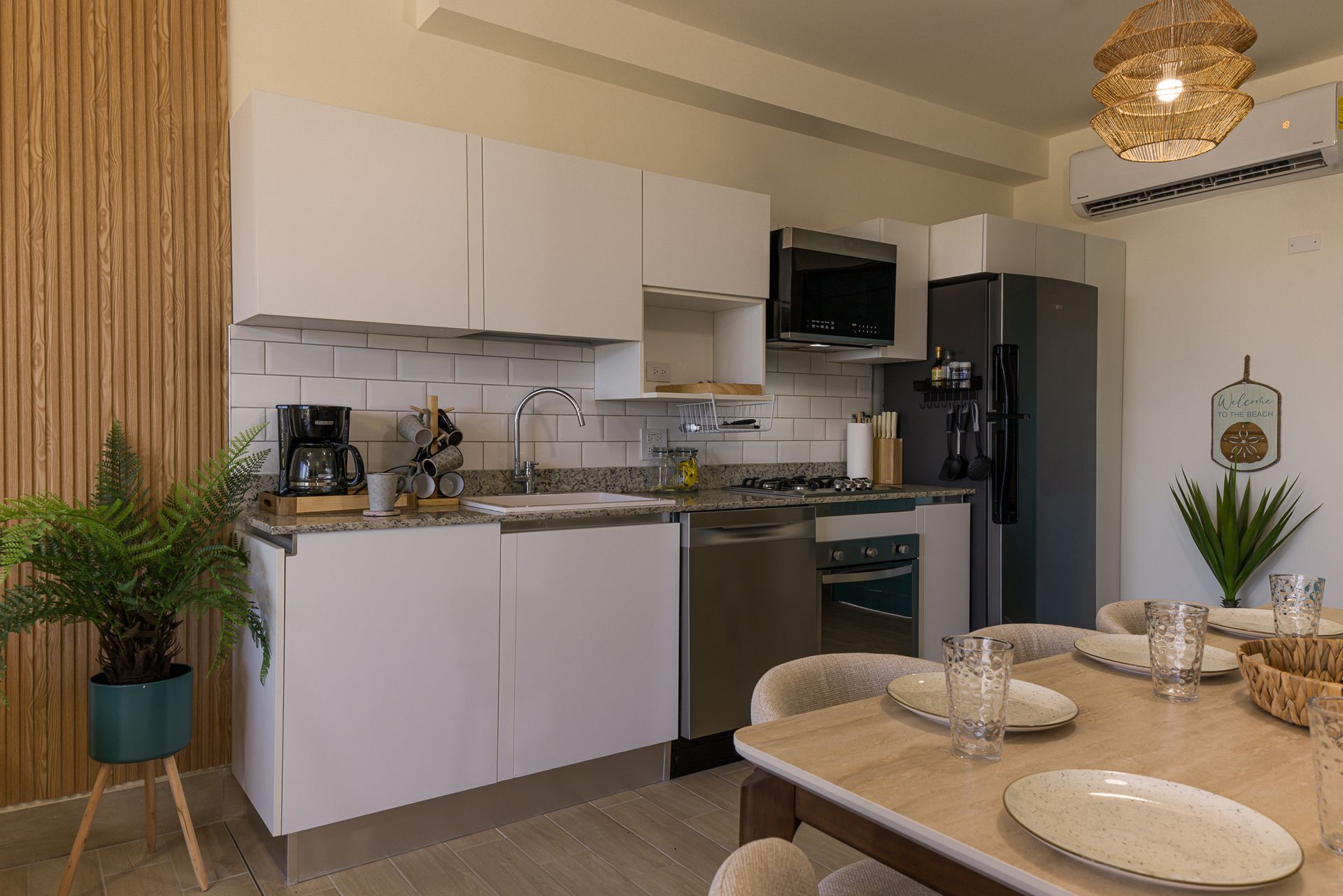 Kitchen of a Playa Caracol apartment with white cabinetry, granite countertops and natural wood paneling, interior design by Furnishing Solutions Panama.