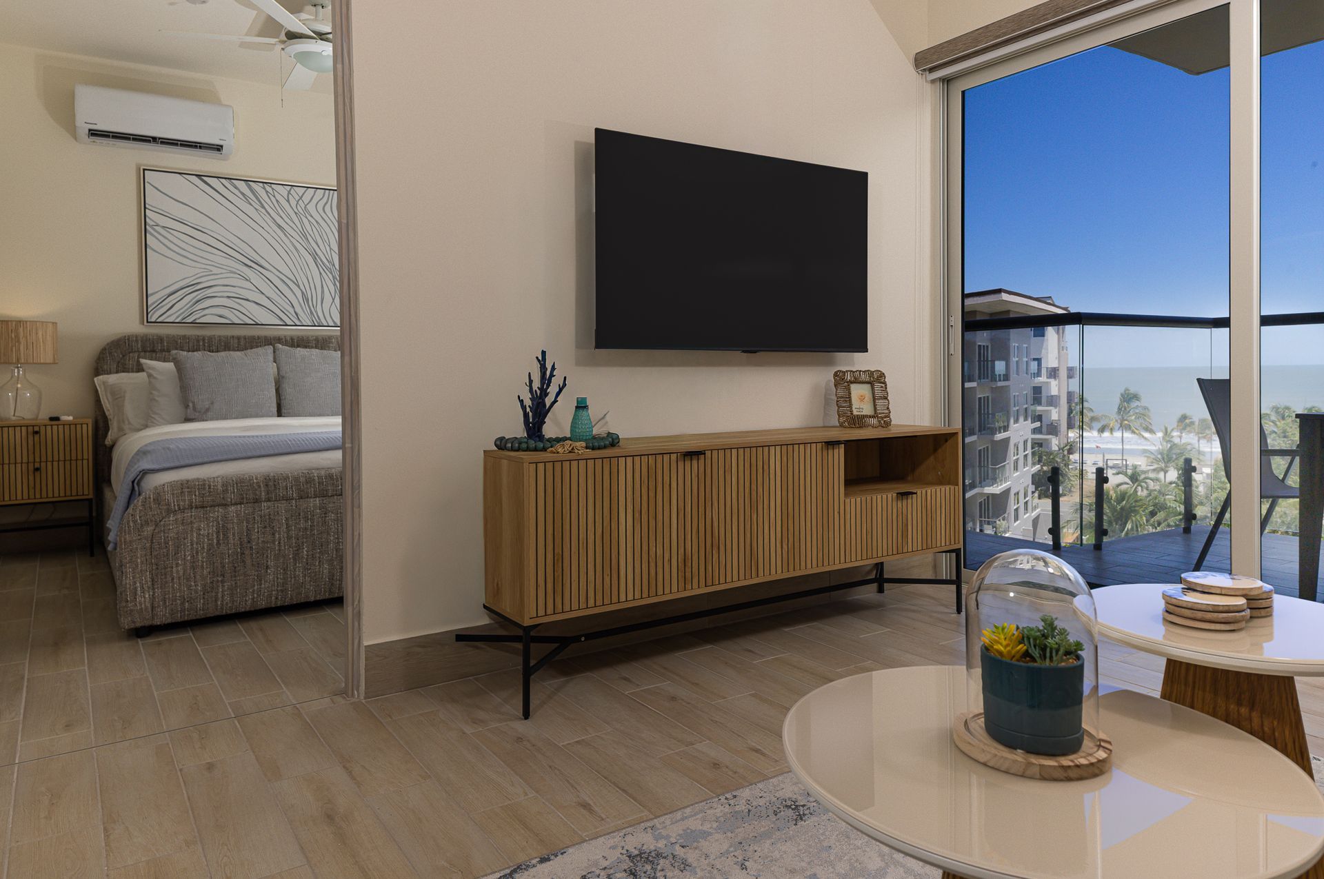 Living area of a Playa Caracol apartment with media console and view to the master bedroom and balcony, interior design by Furnishing Solutions Panama.