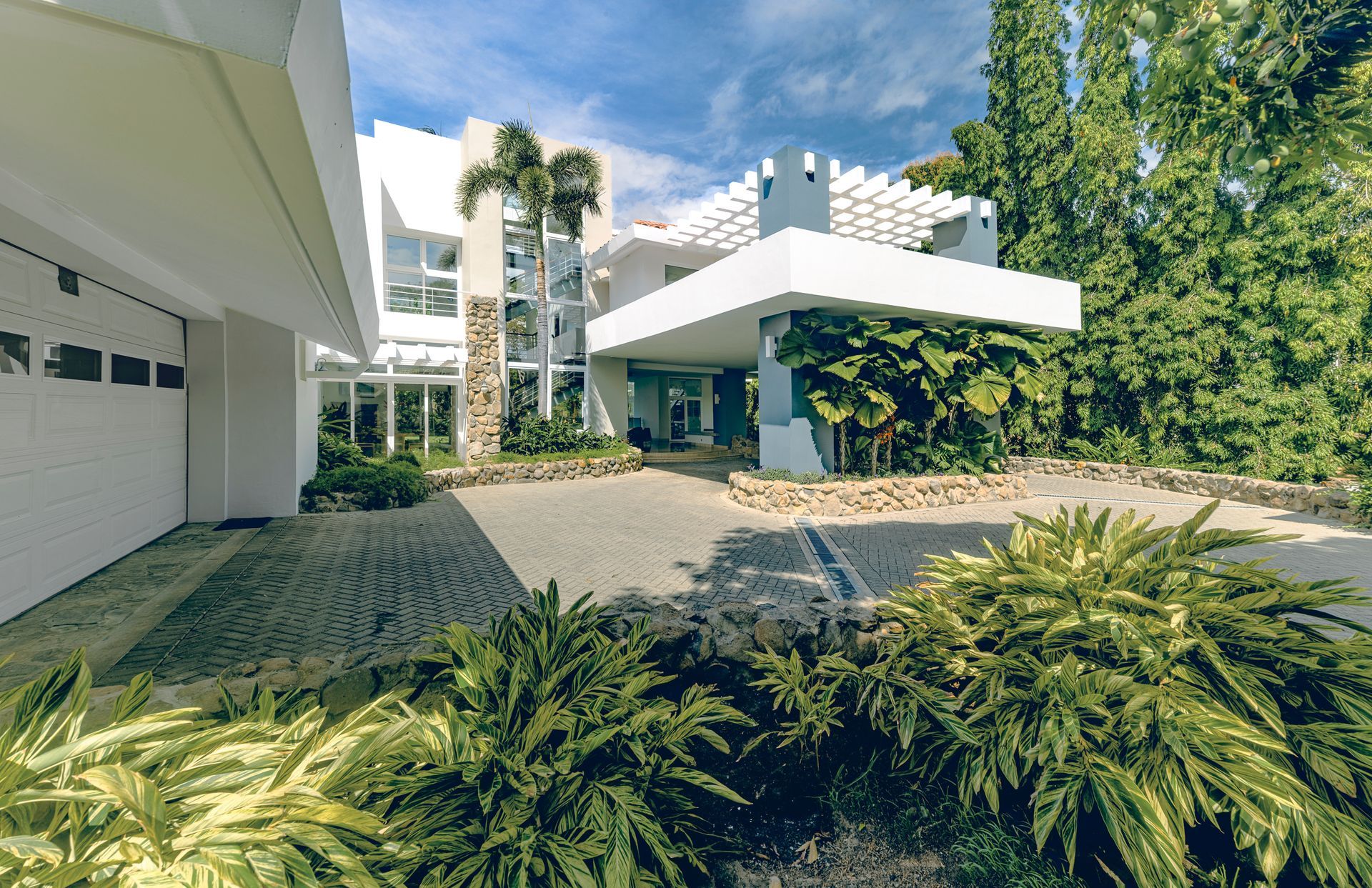 A modern white house with a paved driveway, surrounded by lush green foliage and tropical plants at punta barco