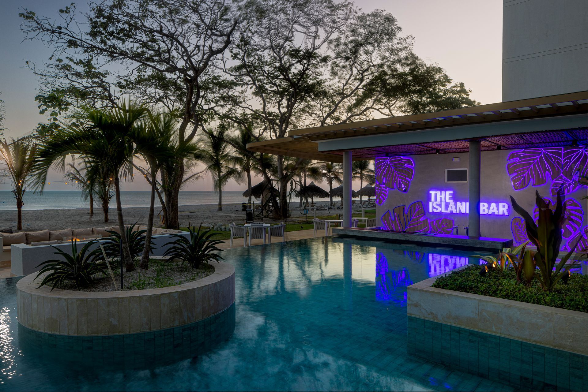 Poolside bar lit with purple lights; beach in background.