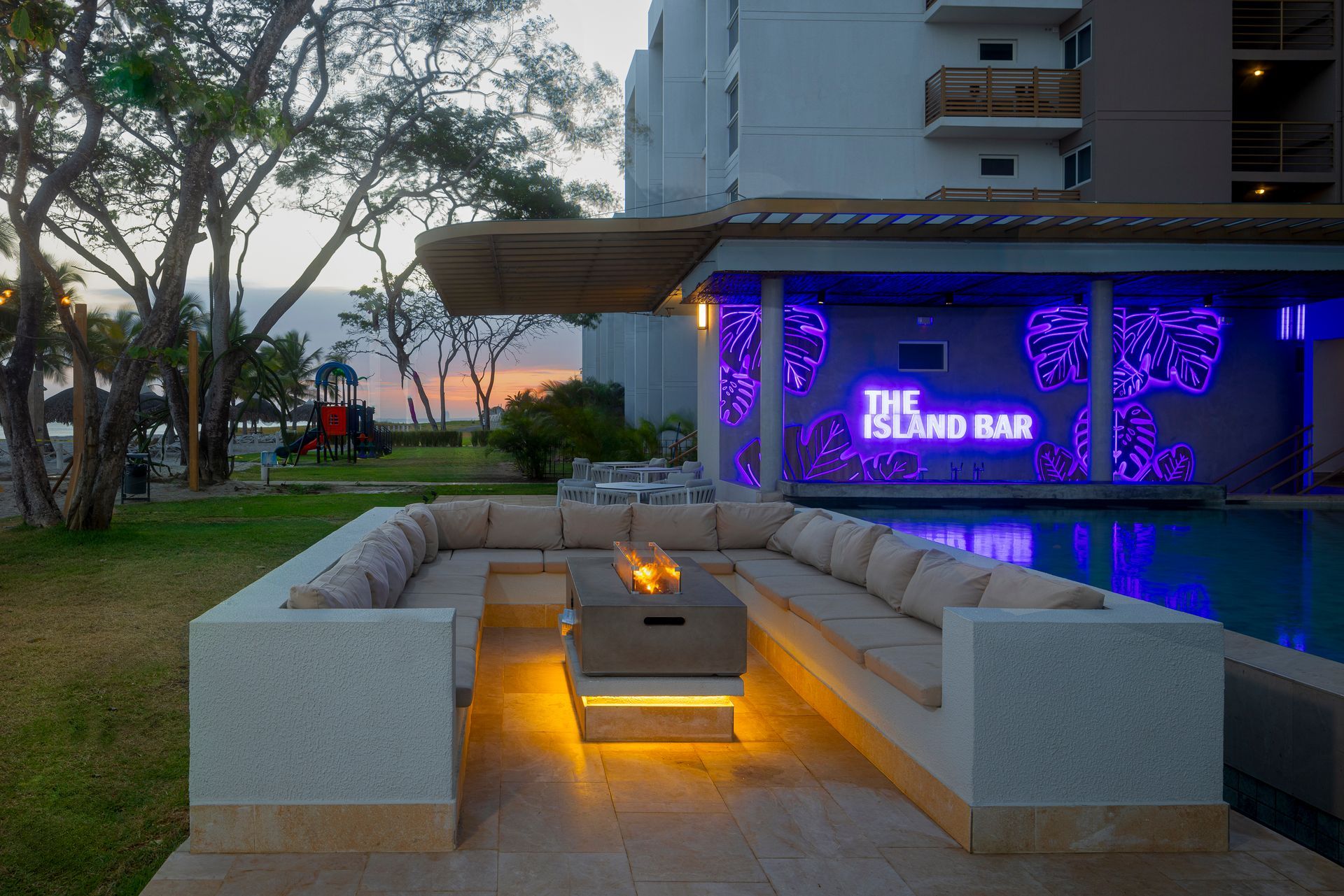 Outdoor bar and lounge area with fire pit, pool, and neon sign