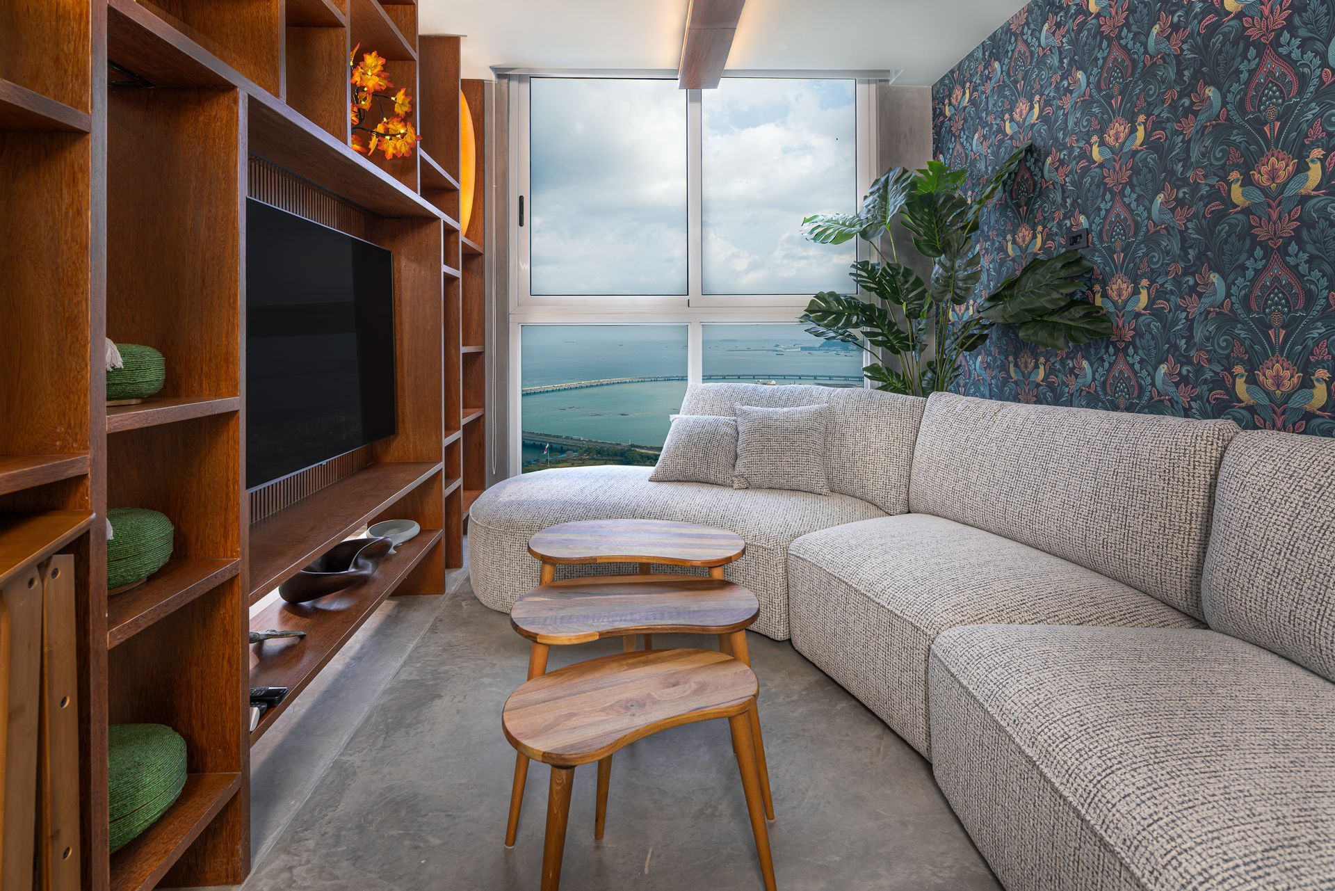 Cozy living room with built-in bookshelves, sectional sofa, small wooden tables, and ocean view through a window.