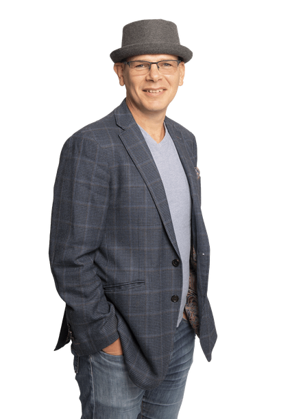 A man wearing a hat and glasses is standing with his hands in his pockets.