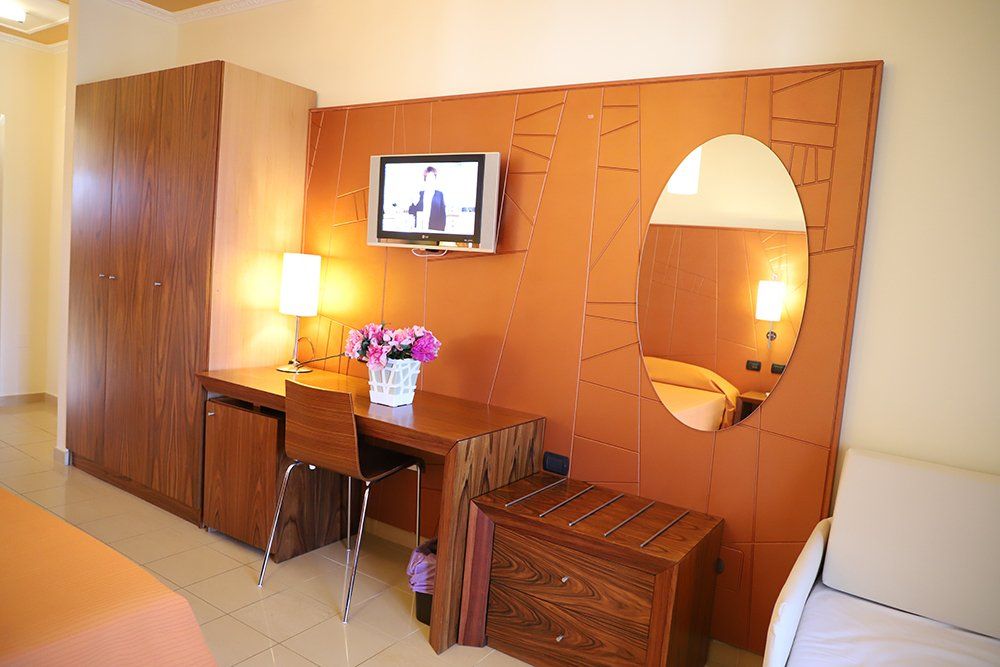 Una stanza d'albergo con una scrivania, sedie, una televisione e uno specchio.
