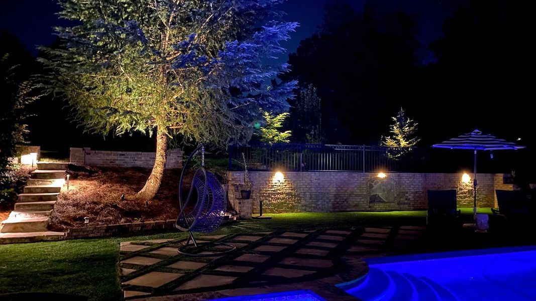 A swimming pool is lit up at night in a backyard.